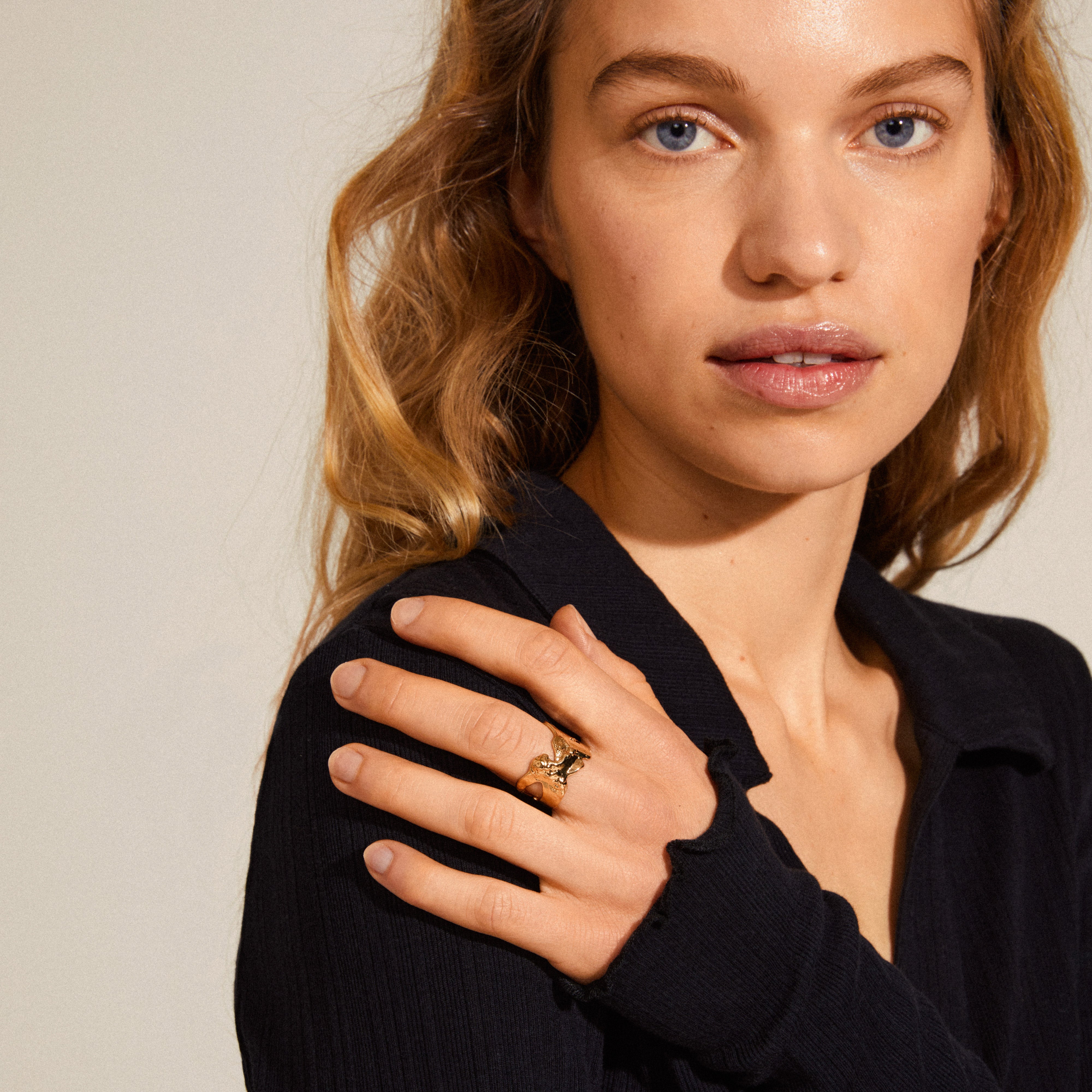 Young woman wearing the COMPASS organic shaped gold-plated ring, featuring a textured, sculptural design inspired by natural landscapes, on her ring finger.