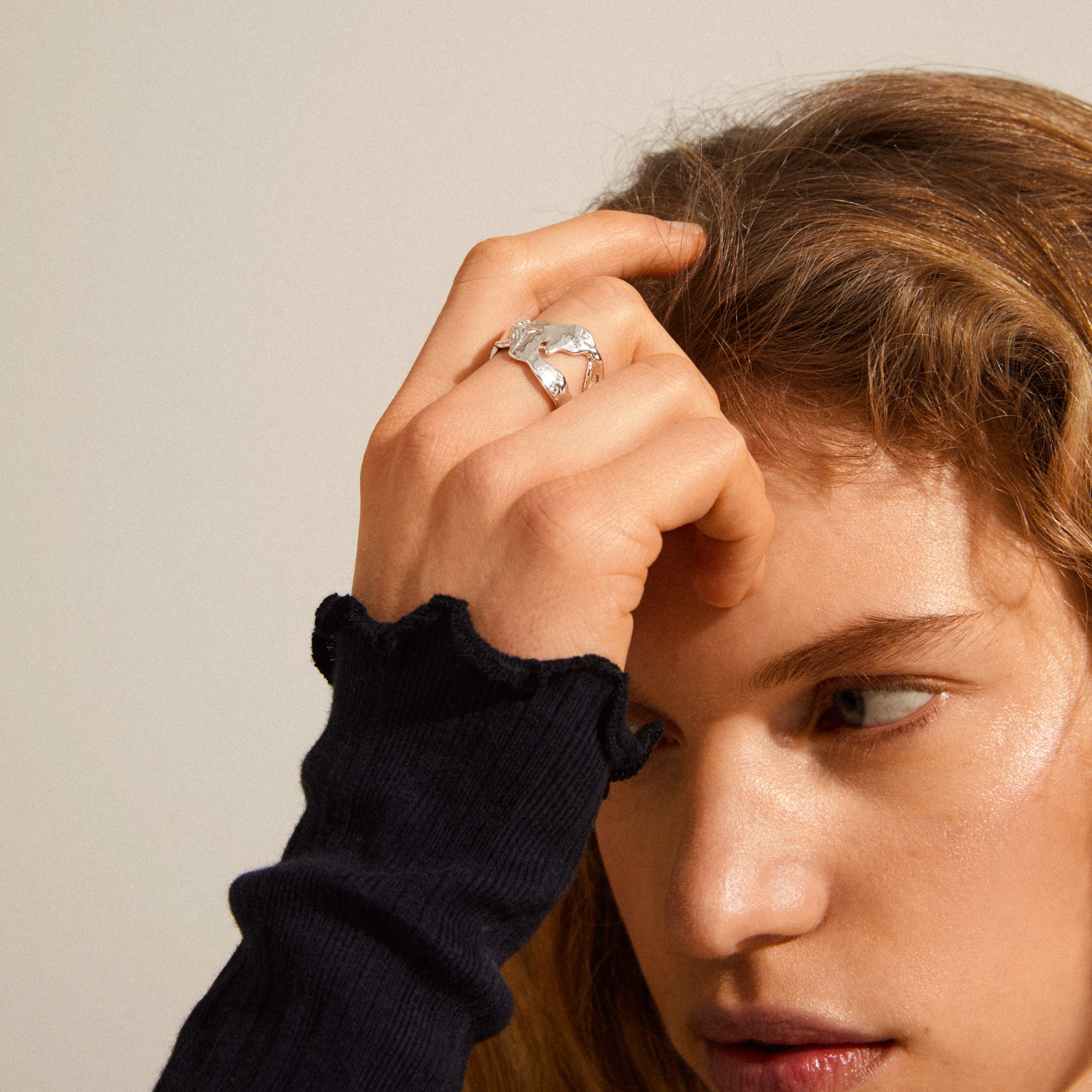 Person wearing Pilgrim's COMPASS silver-plated ring, showcasing its chunky, organic design against a black ribbed top with ruffled cuffs.