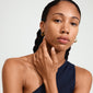 Close-up of a woman wearing Pilgrim's DUNE gold-plated earrings, highlighting their shiny finish and elegant shape. Her hand gently rests on her neck.