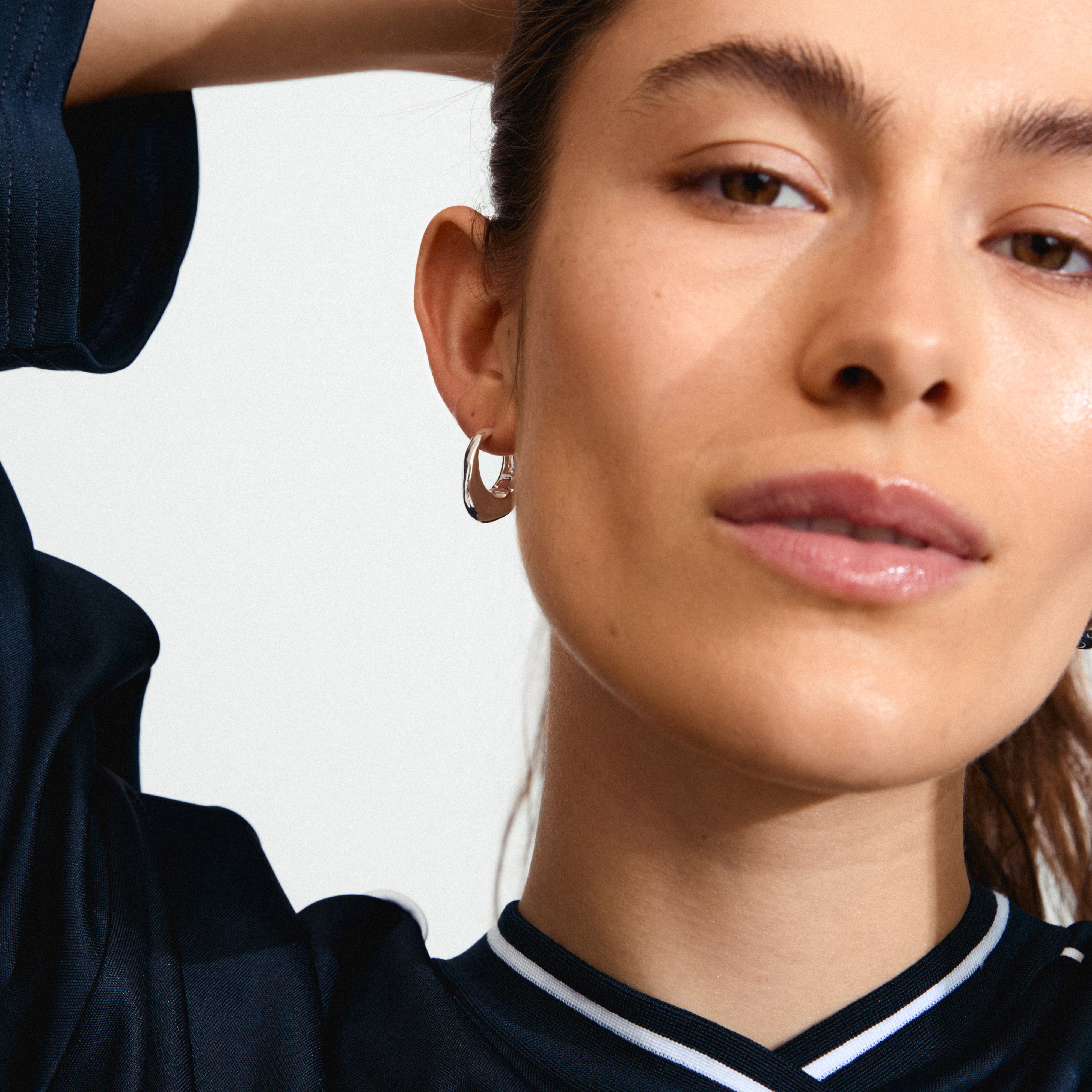 DUNE earrings silver-plated: Close-up of a woman wearing Pilgrim's silver-plated chunky hoop earrings, showcasing their sleek, shiny finish and elegant shape.
