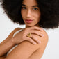 Young woman with an afro displays Pilgrim's FREE ring gold-plated on her finger, showcasing its chunky, organic design in a minimalist, natural-lit setting.