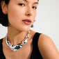 Young woman wearing the FREE statement necklace silver-plated; chunky, asymmetrical, pebble-shaped links with a mirror finish, exuding a playful, ocean-inspired style.