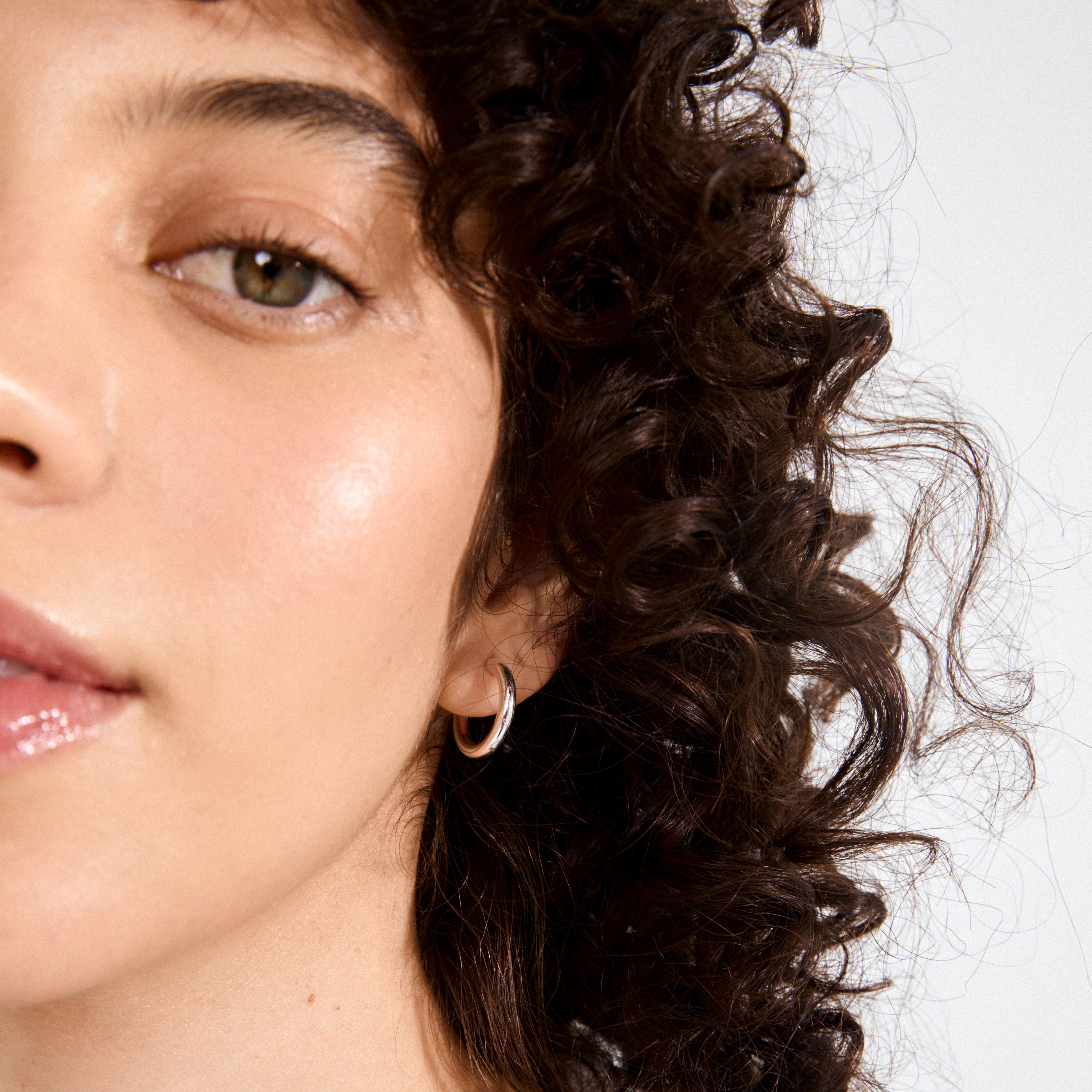 Close-up of a woman wearing DOLAG earrings, silver-plated chunky half hoops, showcasing a bold, timeless look with recycled materials.