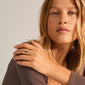 Close-up of a young woman showcasing Pilgrim's HAPPY organic-shaped, gold-plated statement ring, emphasizing its Nordic-inspired, sculptural design on her finger.