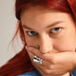 Young person with long red hair covers mouth, showcasing Pilgrim's HAPPY silver-plated, organic-shaped ring on middle finger, highlighting its chunky, sculptural design.