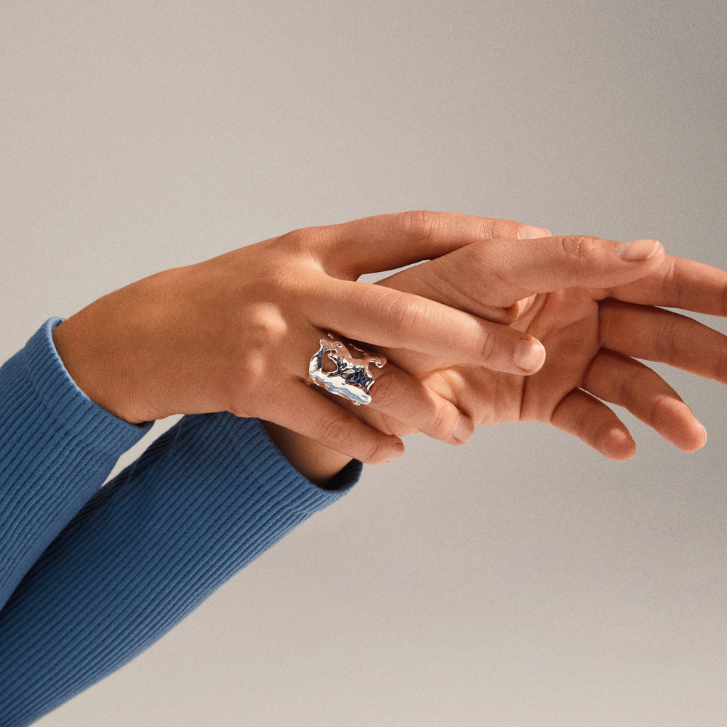 Two hands gently clasp; the upper hand wears the HAPPY organic shaped ring, silver-plated with a molten-metal look, highlighting its unique, handcrafted design.