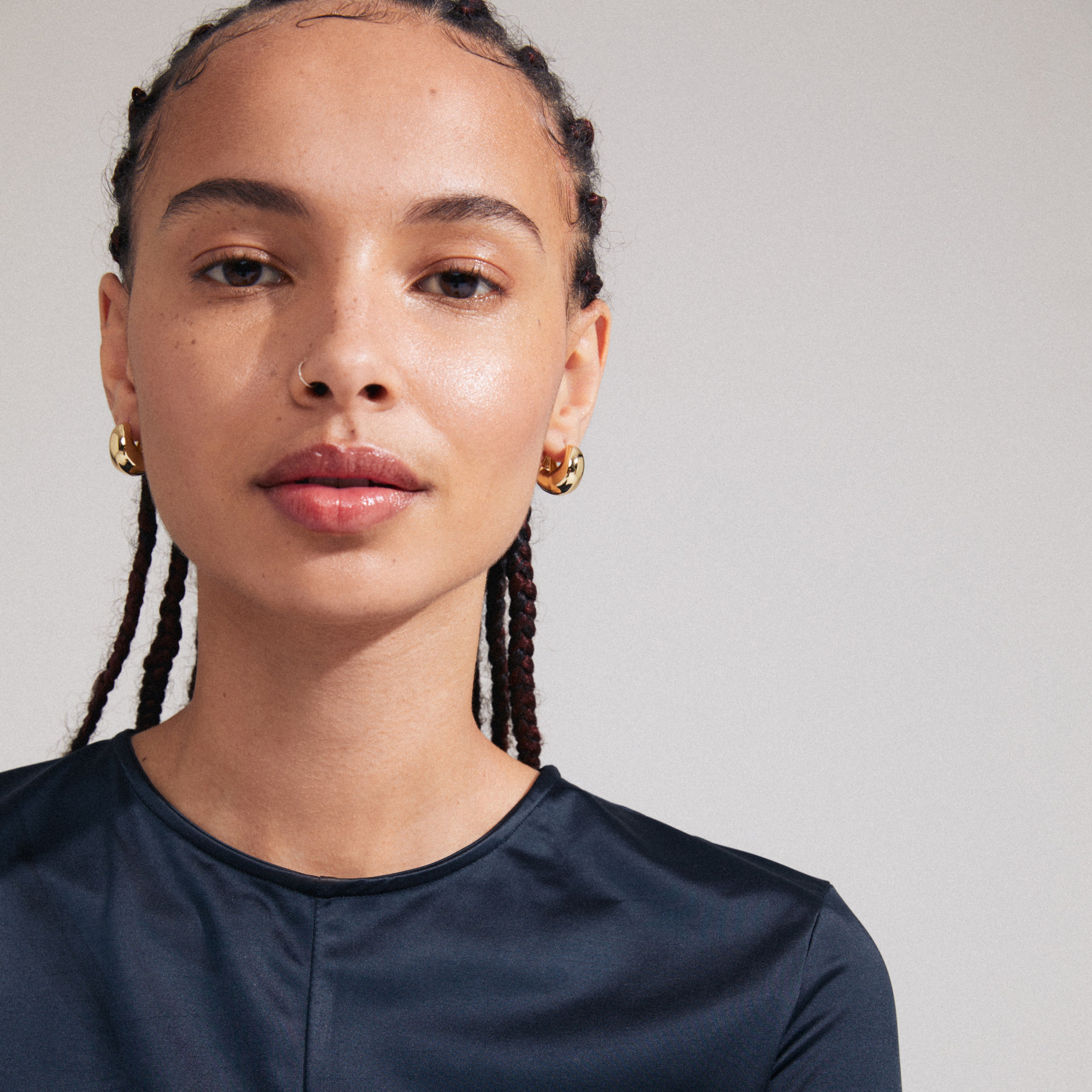 Woman wearing Pilgrim's LIGHT chunky gold-plated earrings, featuring wavy Scandinavian-inspired design and click clasp, highlighting her braided hairstyle and radiant expression.