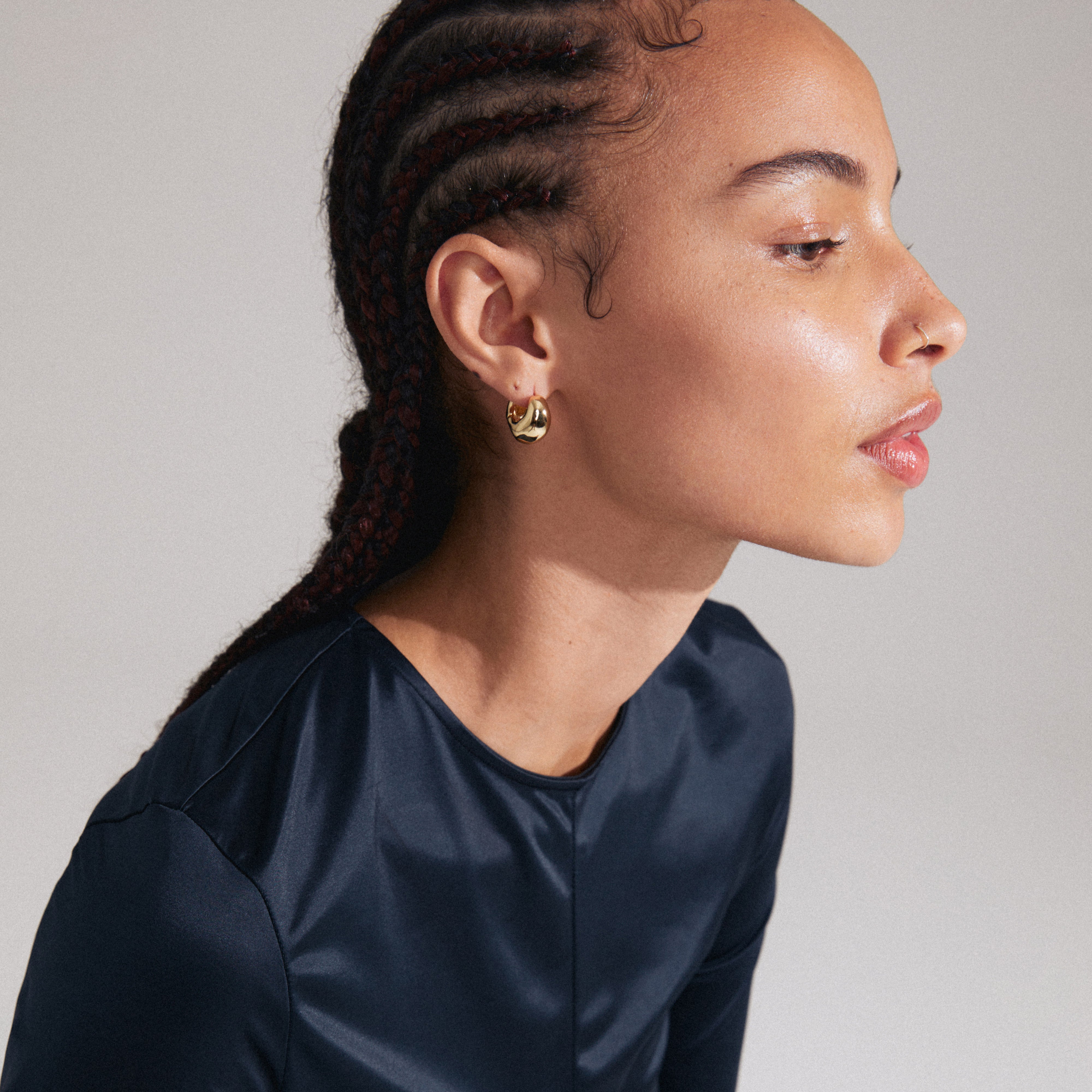 Woman with braided hair wearing LIGHT chunky gold-plated earrings from Pilgrim. The earrings feature unique wavy shapes and a click clasp design.