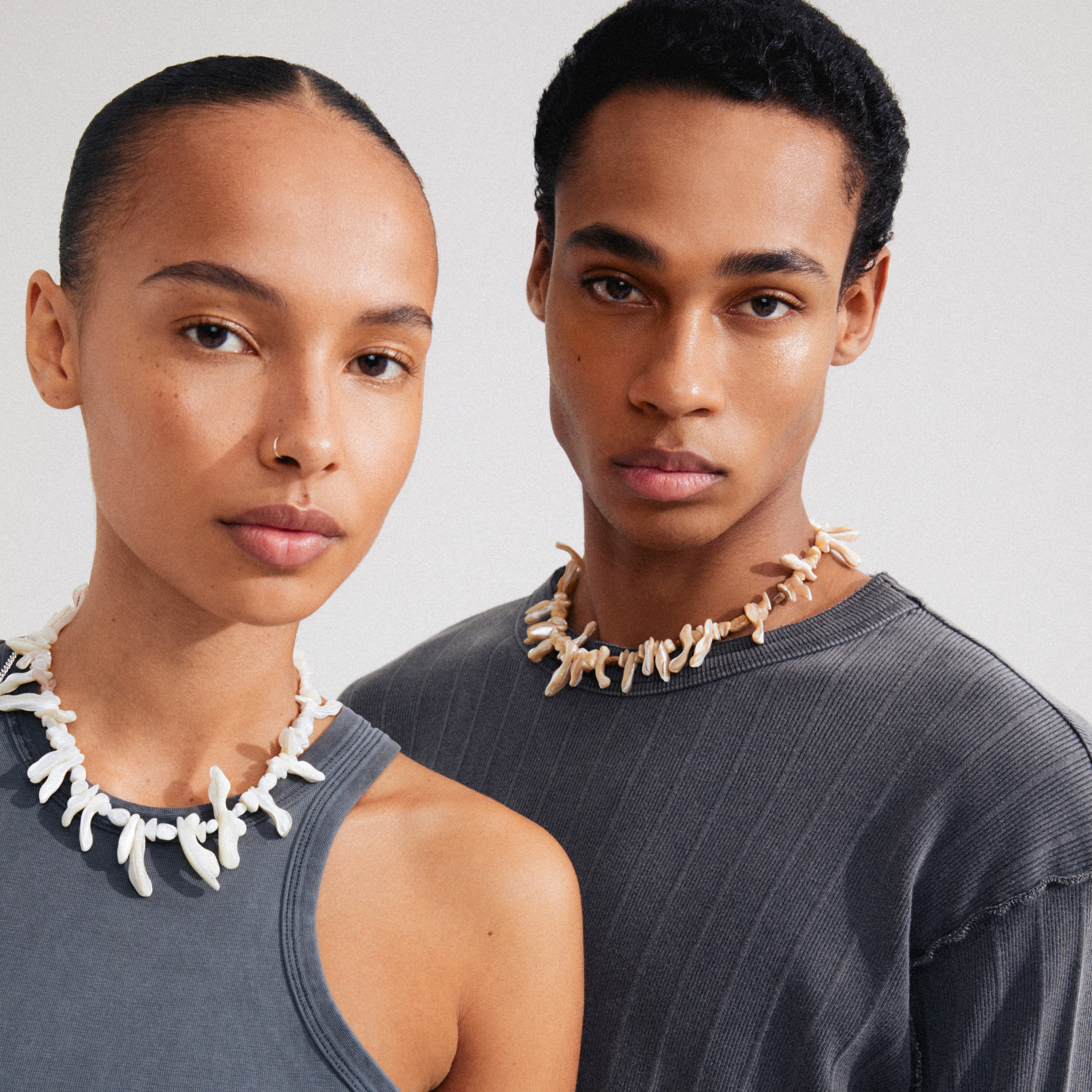 Man and woman showcasing the LIGHT seashell necklace by Pilgrim, featuring irregular mother-of-pearl pieces and a gold-plated extension chain for adjustable length.