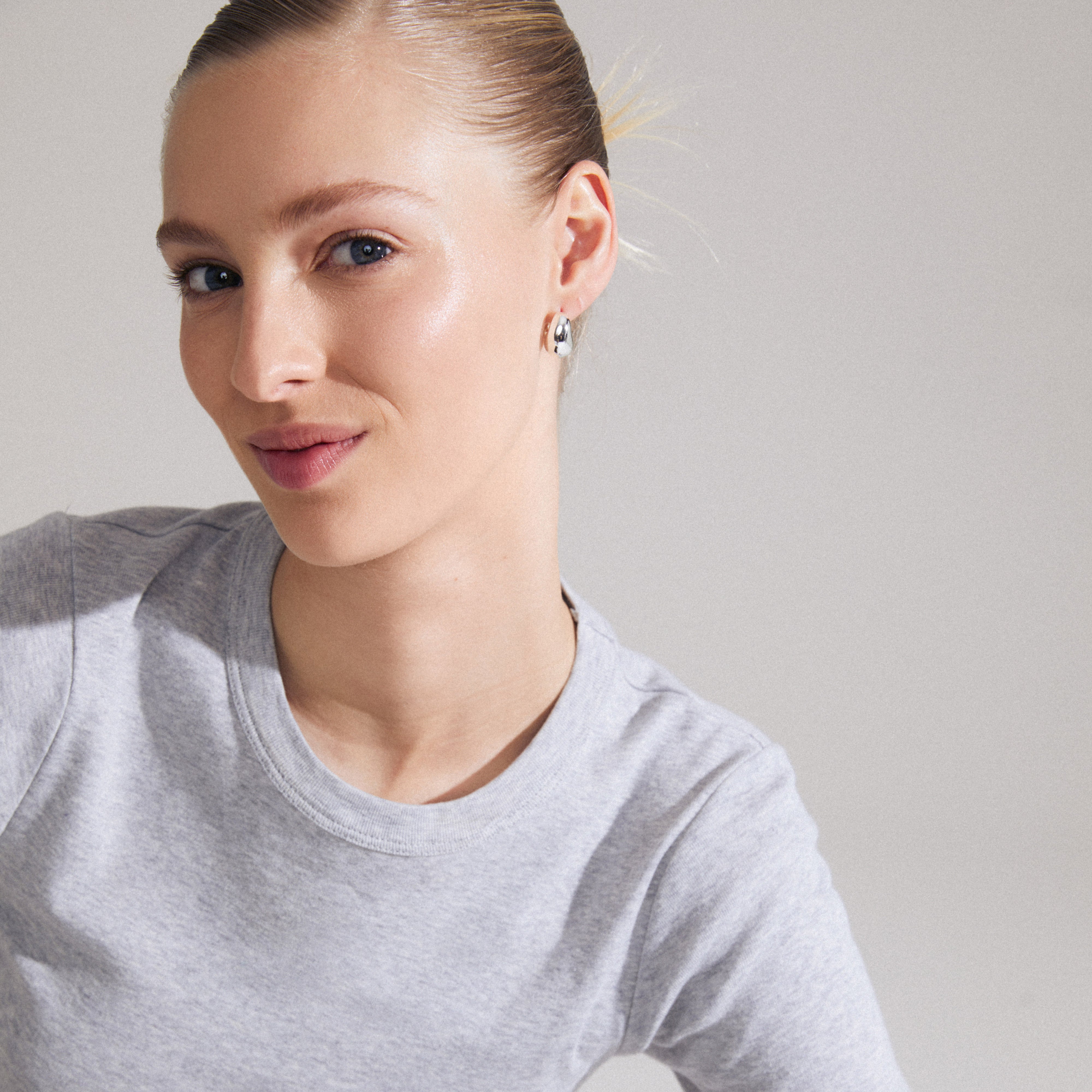 Woman smiling, wearing Pilgrim's LIGHT chunky earrings silver-plated, showcasing ultra chunky, wavy hoops inspired by Scandinavian design, styled effortlessly for a relaxed look.