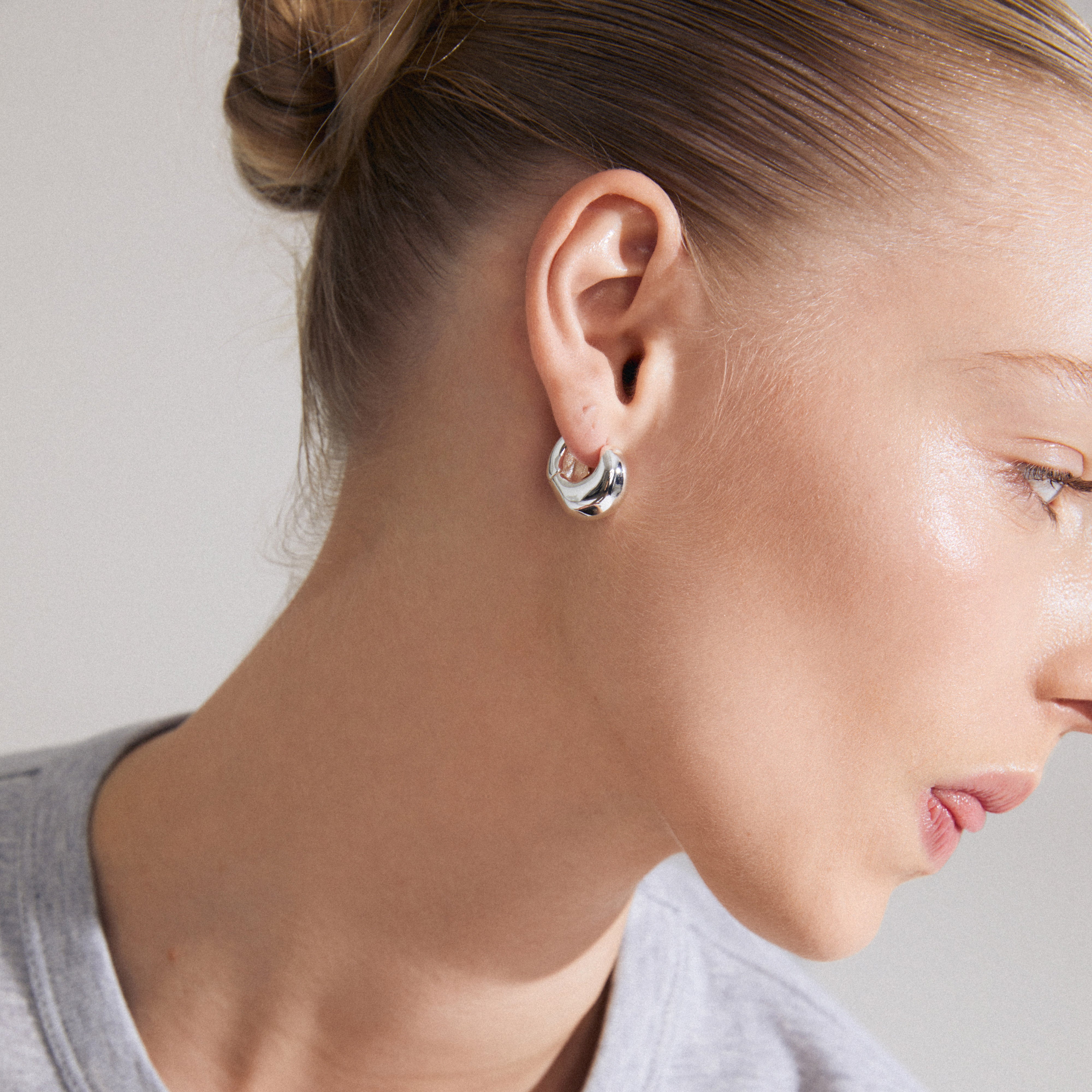 Close-up of a woman's ear wearing LIGHT chunky silver-plated earrings from Pilgrim's LIGHT collection, showcasing unique wavy-designed hoops with an easy click clasp.
