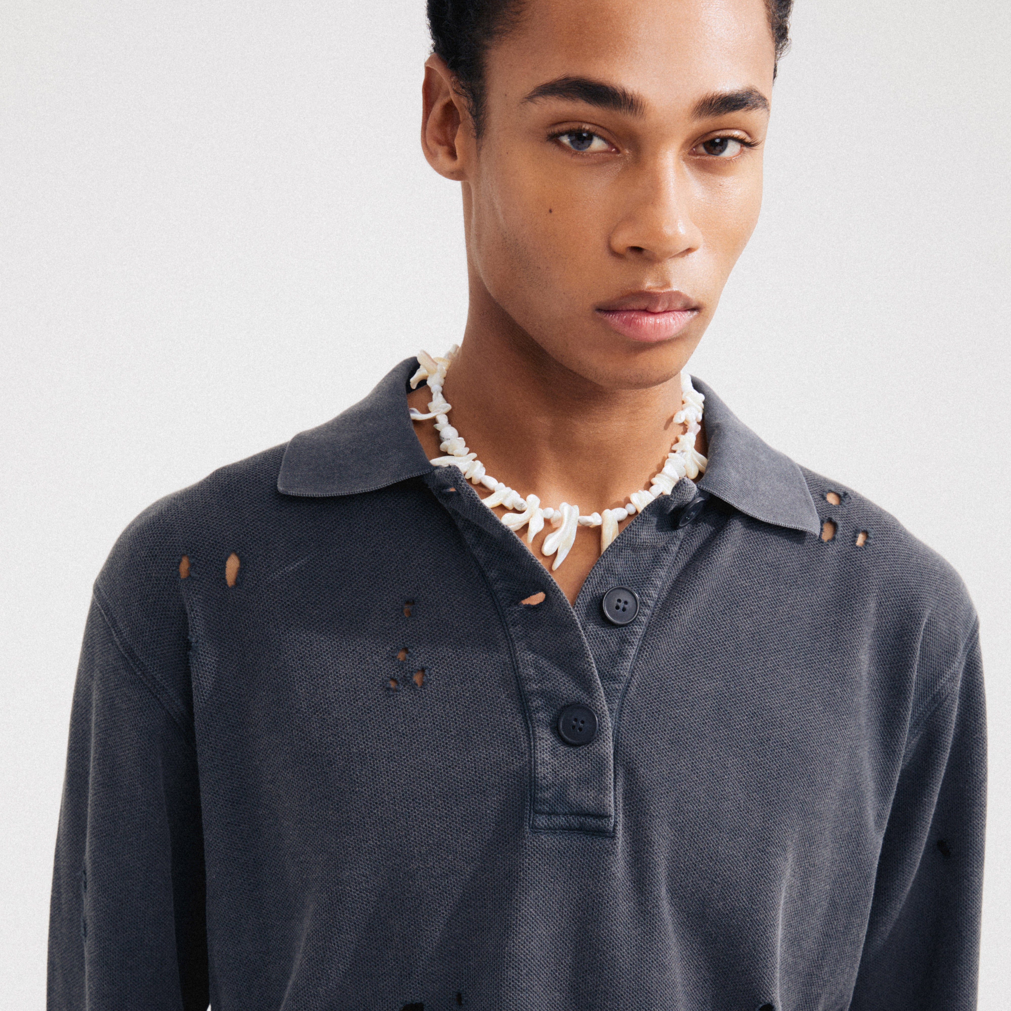 Man wearing Pilgrim's LIGHT seashell necklace, featuring irregular mother-of-pearl pieces, silver-plated chain, and semi-precious stones, exuding boho luxe vibes.