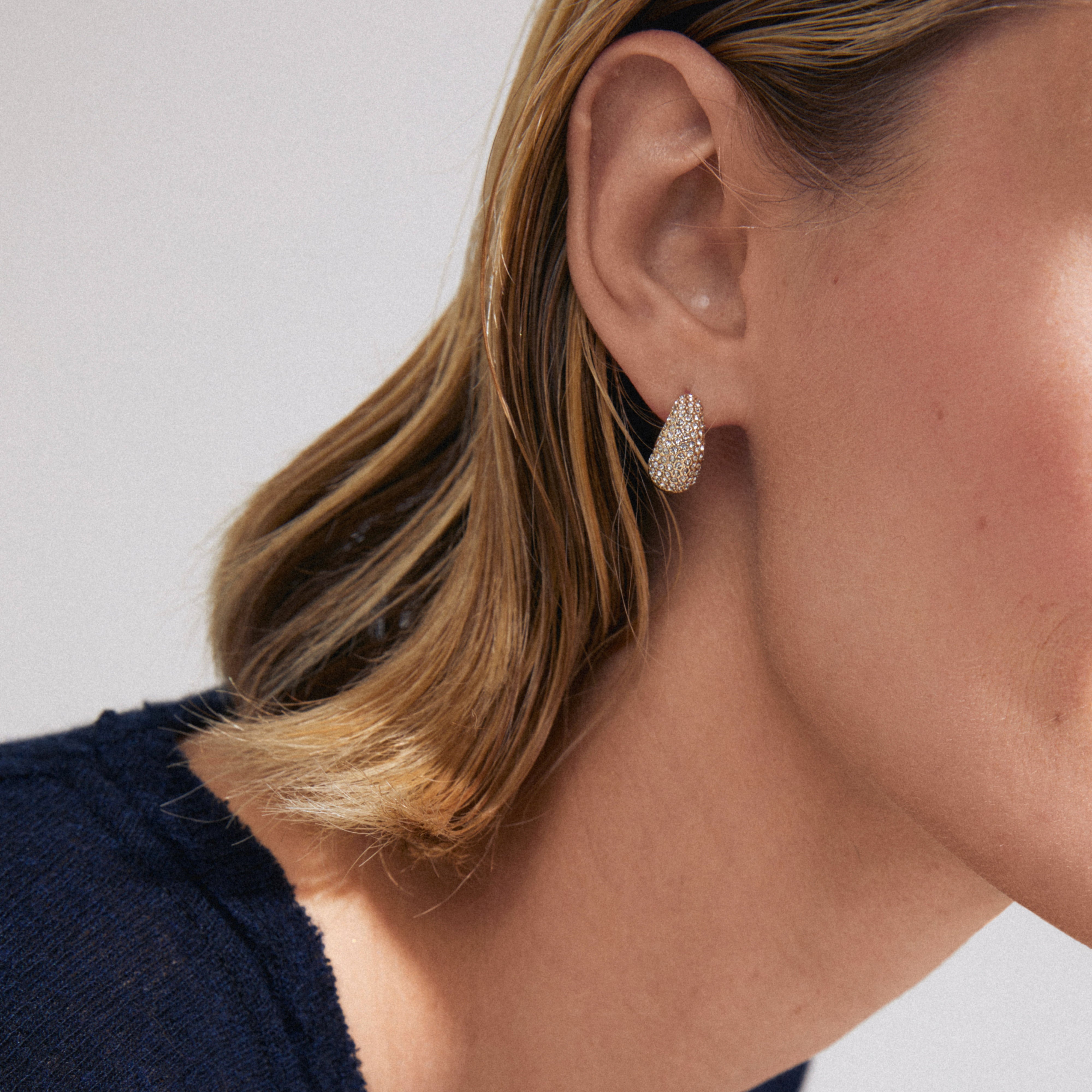 Person wearing Pilgrim's FOCUS gold-plated crystal earrings with pavé-style teardrop design, showcasing sparkling stones and a sleek finish against short blonde hair.