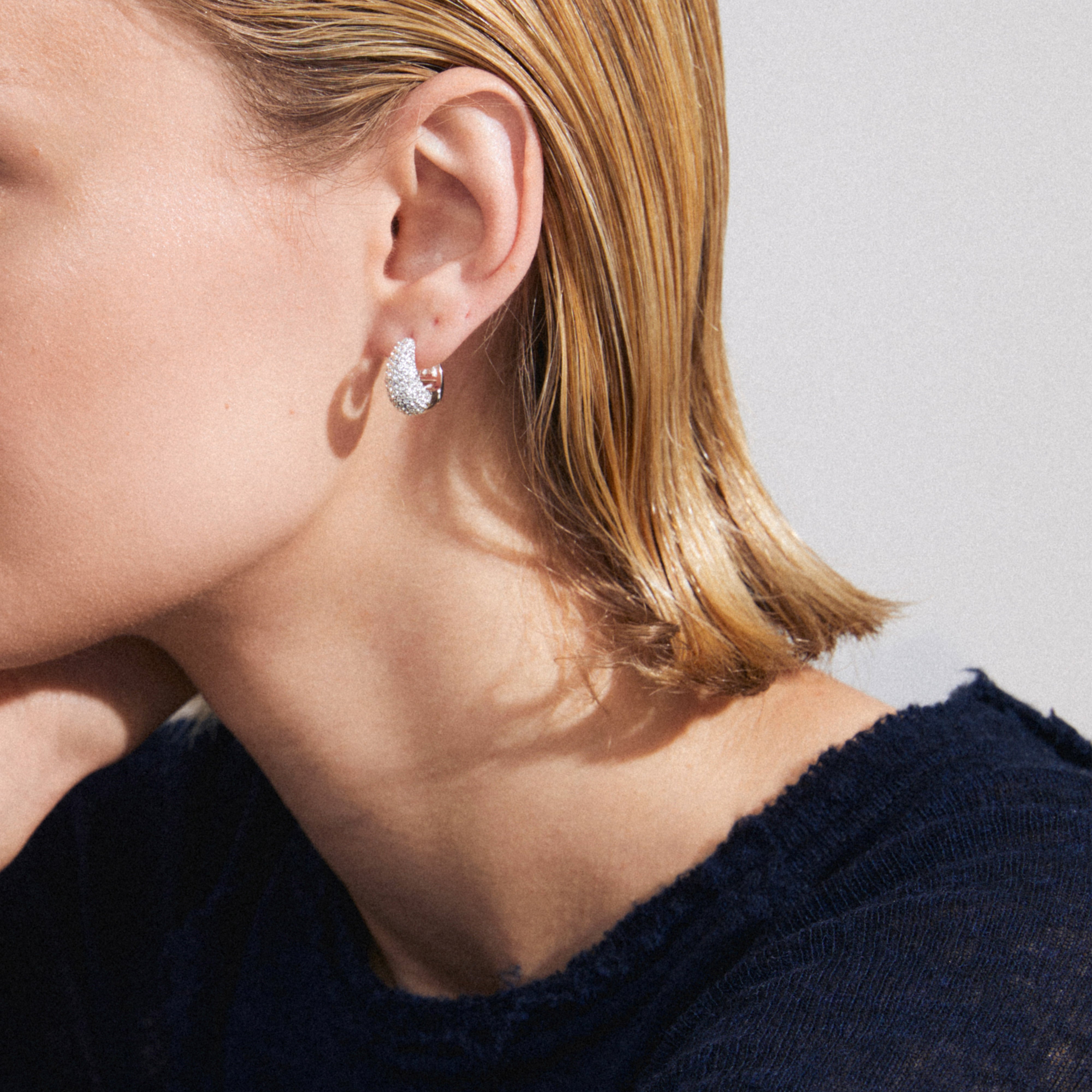 Woman wearing Pilgrim's FOCUS crystal earrings, silver-plated with sparkling stones, showcasing a sophisticated, chunky hoop design for a glamorous, eco-conscious style.