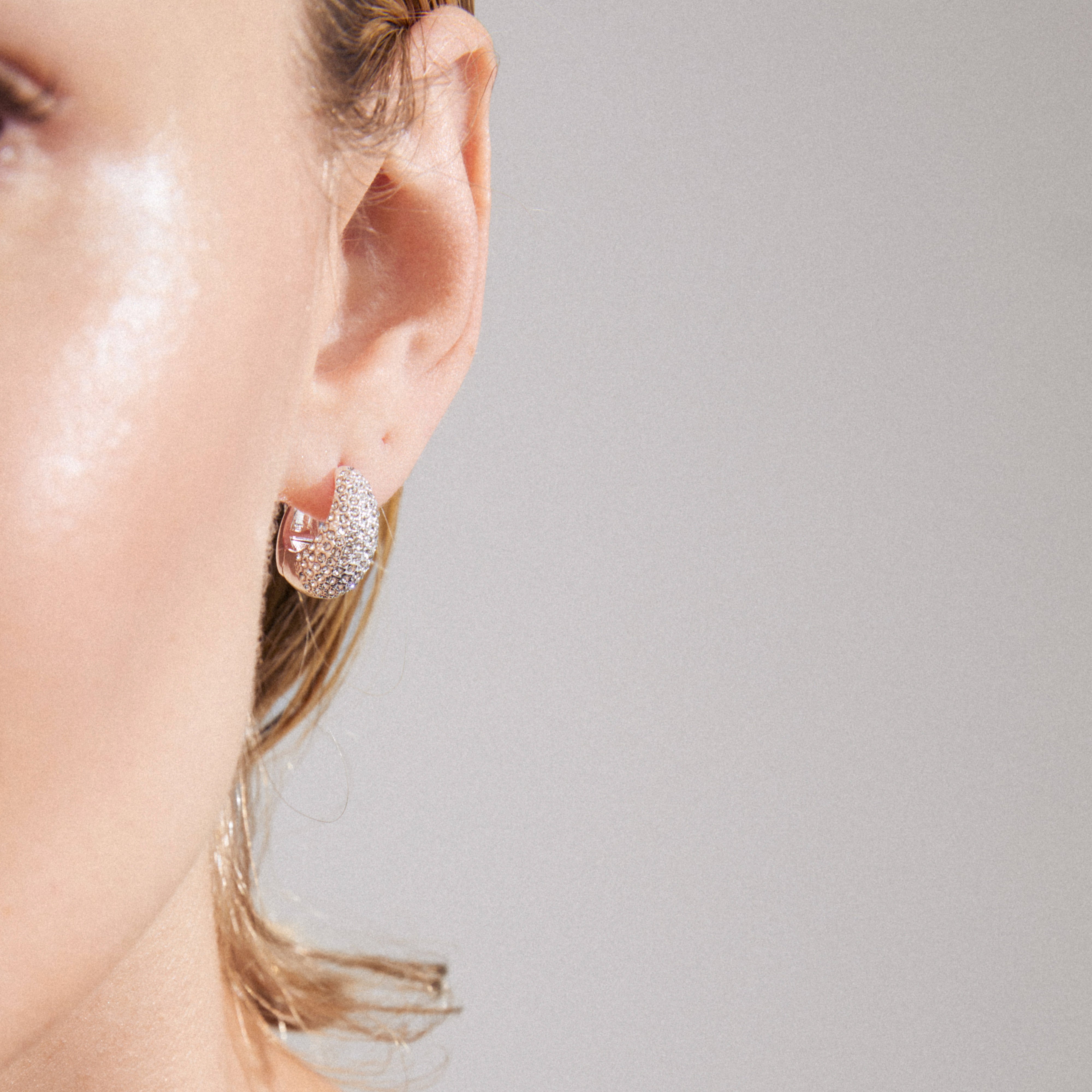 Close-up of a person's ear wearing Pilgrim's FOCUS crystal earrings, silver-plated with sparkling Preciosa crystals, showcasing a chunky, sophisticated design.