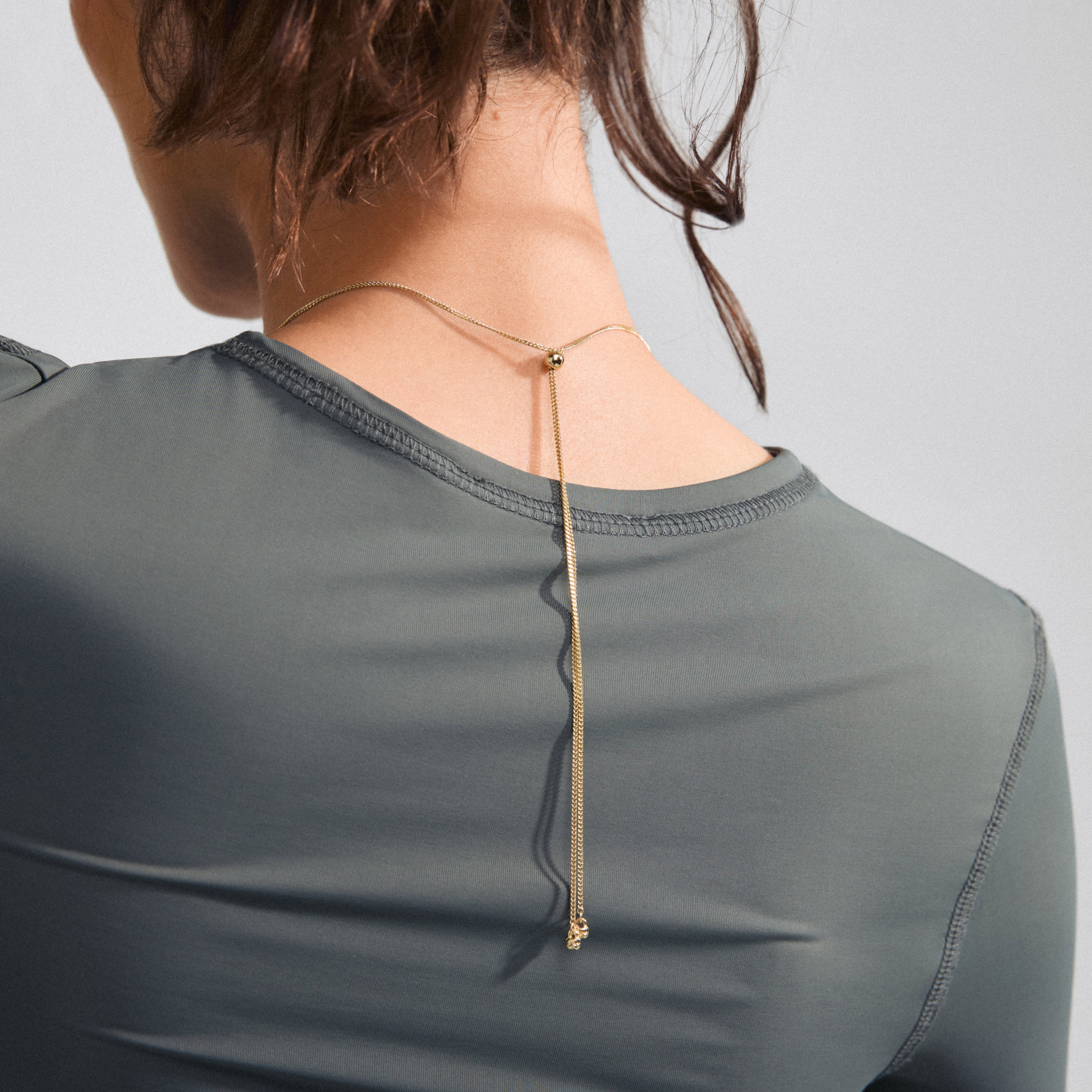 Woman wearing BELIEVE necklace gold-plated from Pilgrim, featuring a slim chain with an organic pendant, adjustable length for a personalized style.