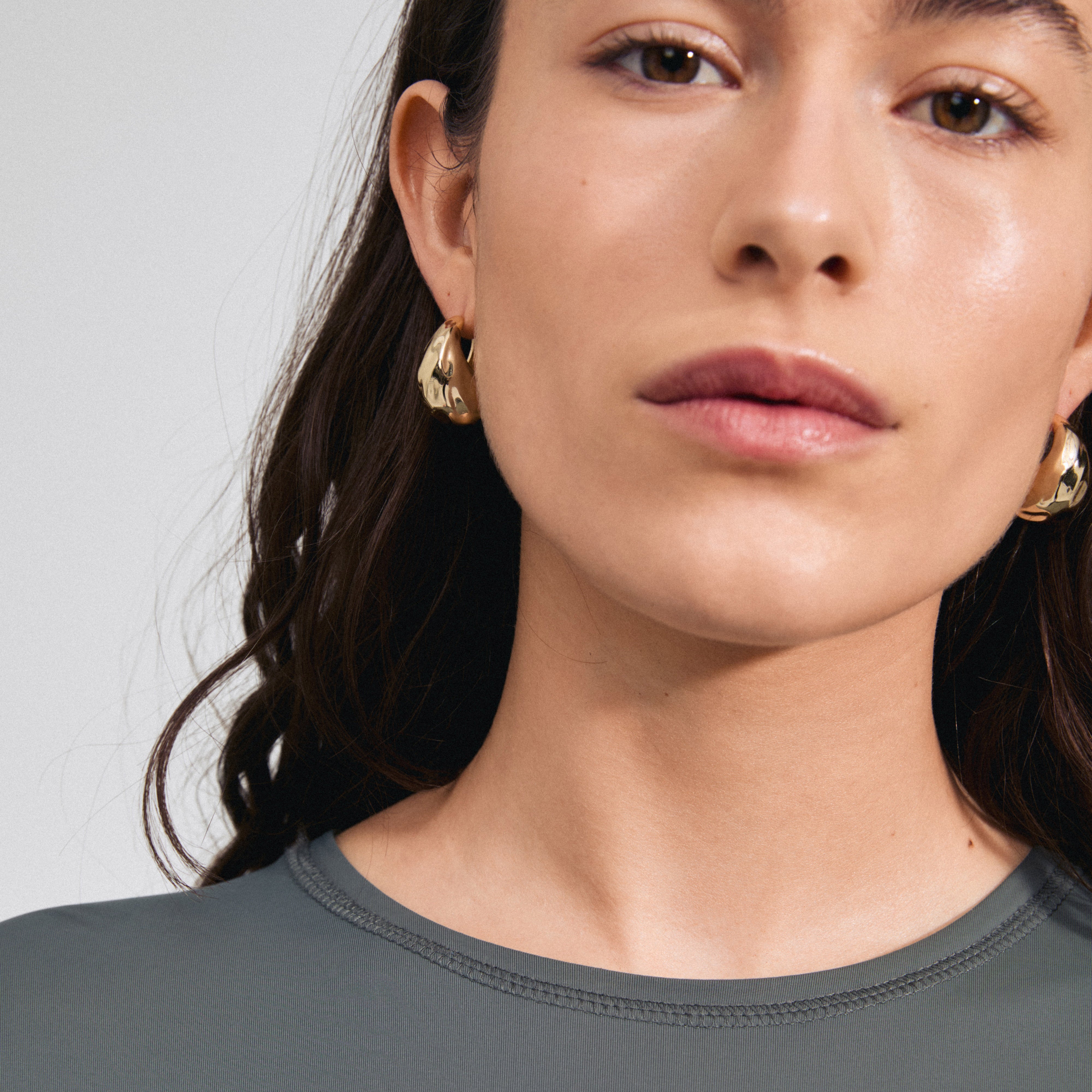 BELIEVE chunky hoop earrings gold-plated, featuring a hammered texture and shiny finish, worn by a woman with long brown hair, highlighting Pilgrim's stylish craftsmanship.