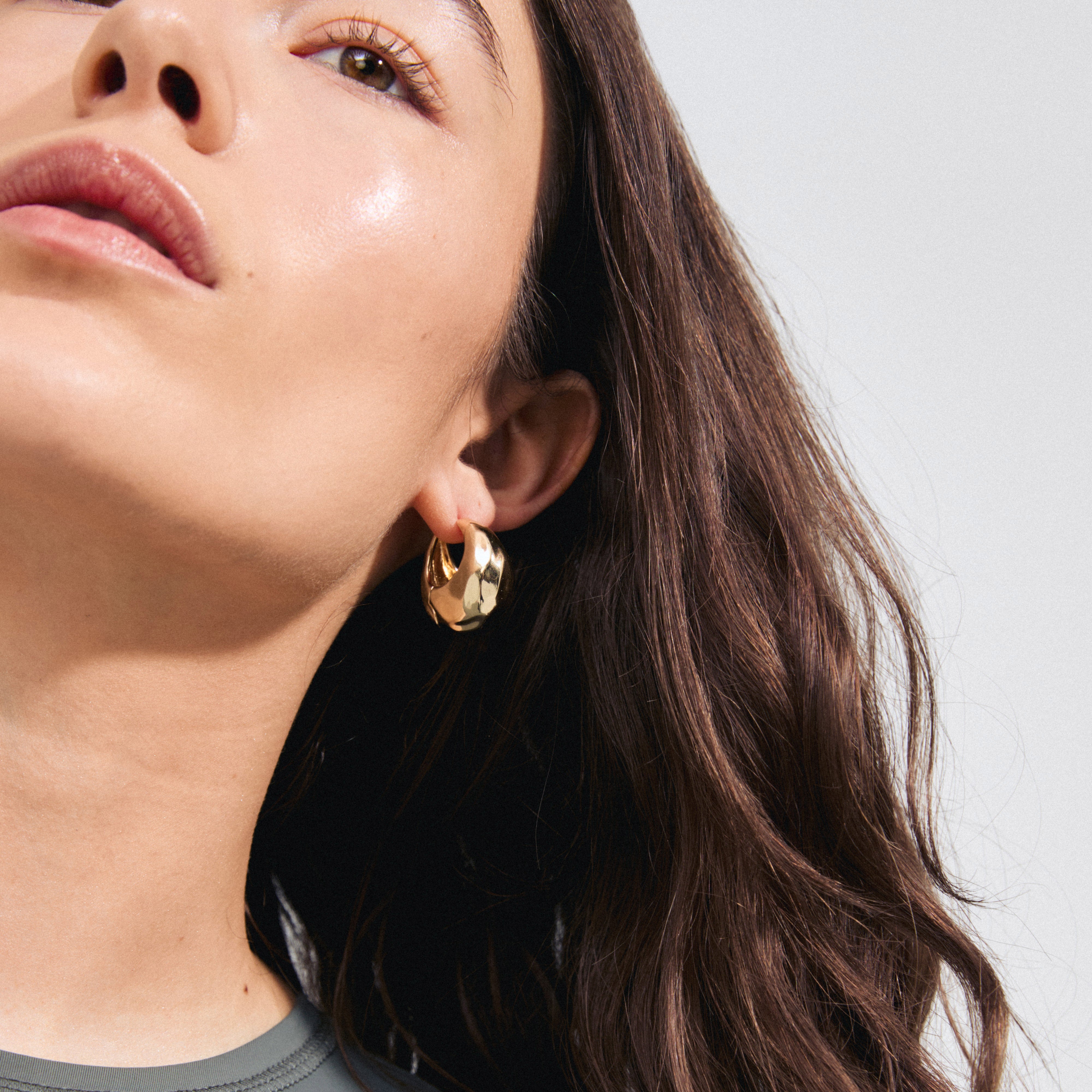 BELIEVE chunky hoop earrings gold-plated, with a shiny hammered texture, worn by a woman. These stylish, recycled hoops enhance everyday elegance with ease.