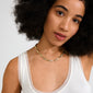 Young woman wearing Pilgrim's INSTANT necklace gold-plated with textured, flat rectangular links, highlighting its chic, handcrafted aesthetic against a plain background.