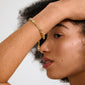 Young person with arm raised, showcasing the Pilgrim INSTANT bracelet: a gold-plated, textured chain with flat links, embodying a raw, chic elegance.