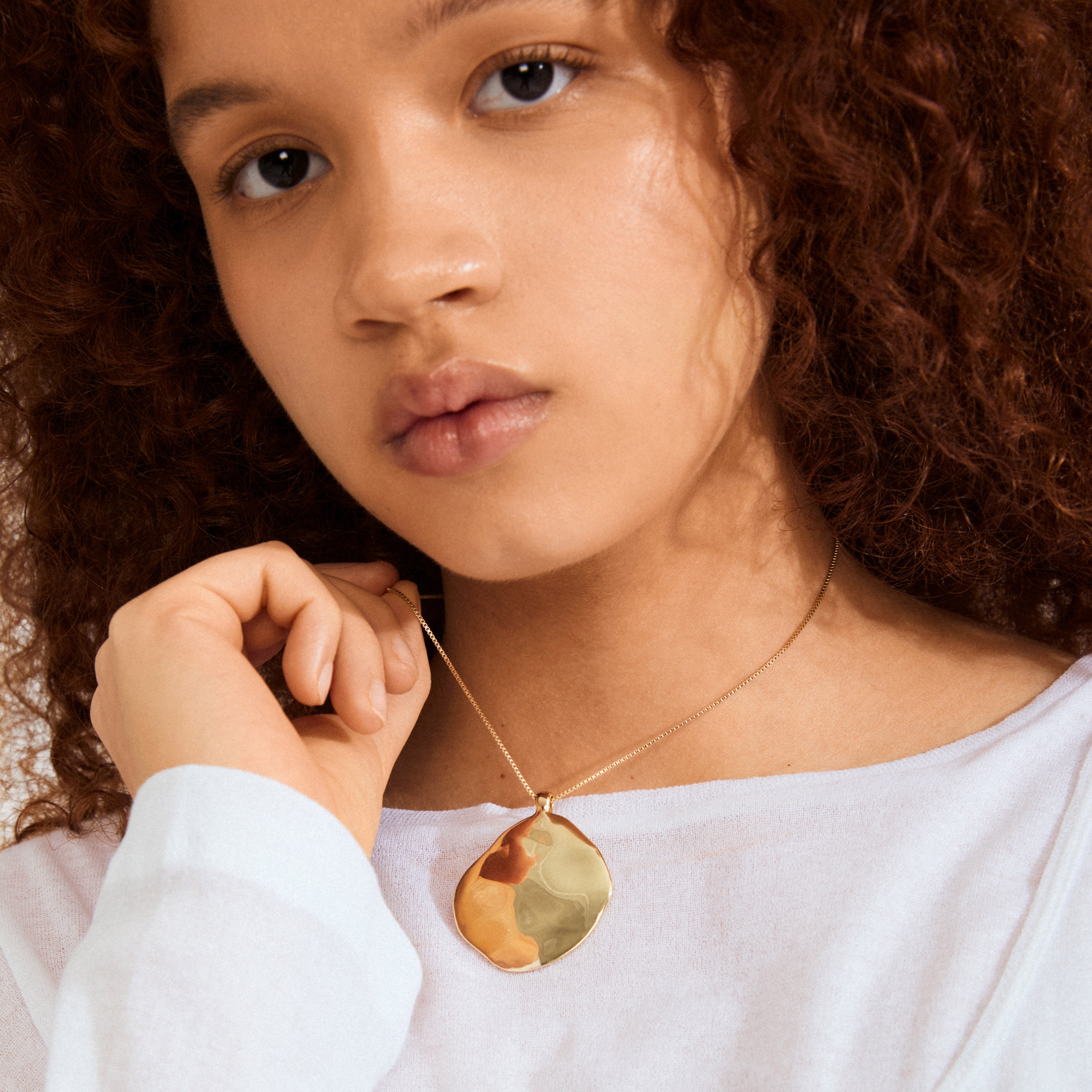 Close-up of Pilgrim's SPARKLE necklace, gold-plated with a hammered-metal pendant, worn on a young person with curly hair, showcasing its ocean-inspired design.