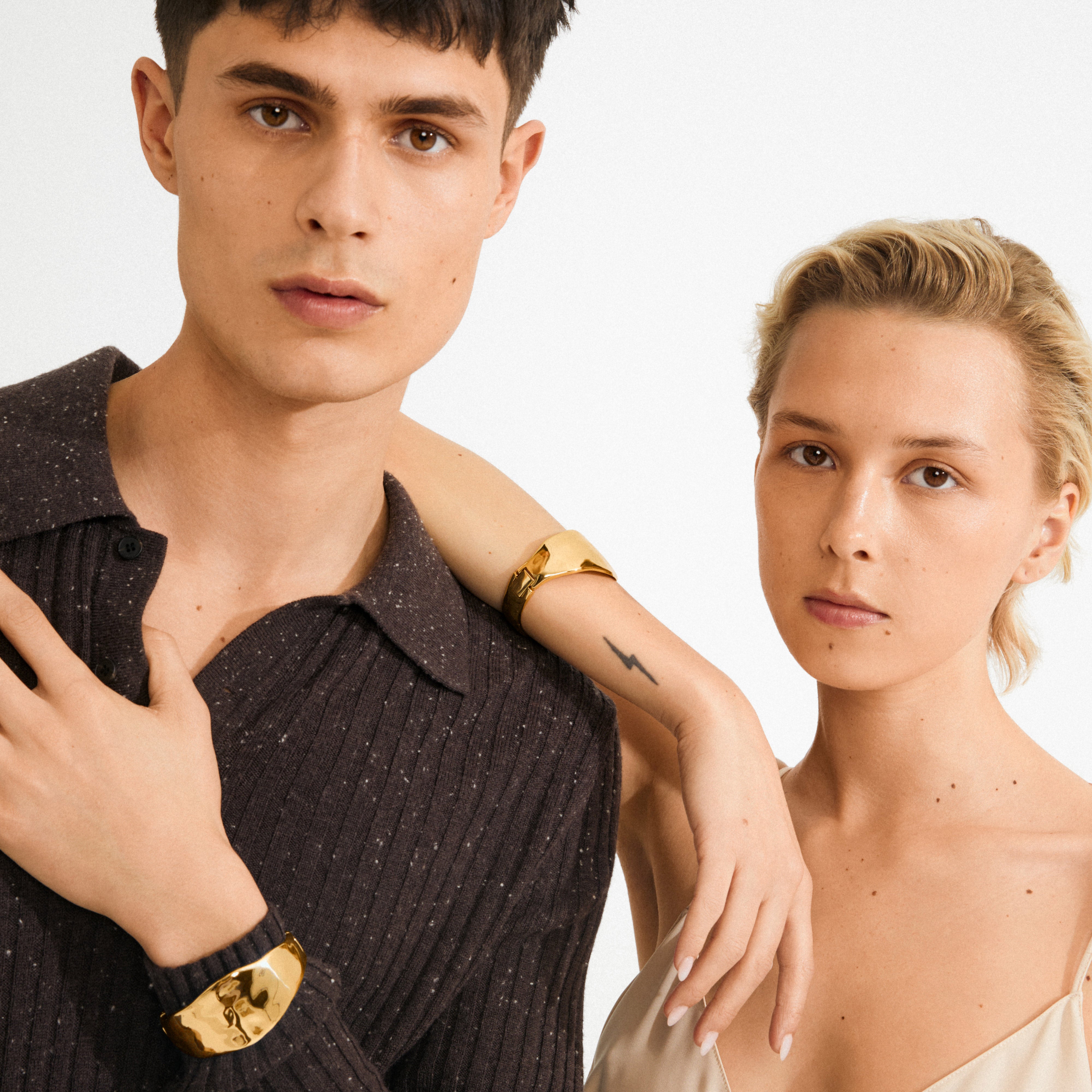 Two young adults showcasing the SPARKLE bracelet gold-plated by Pilgrim, emphasizing its sleek, polished design and minimalist Scandinavian style.