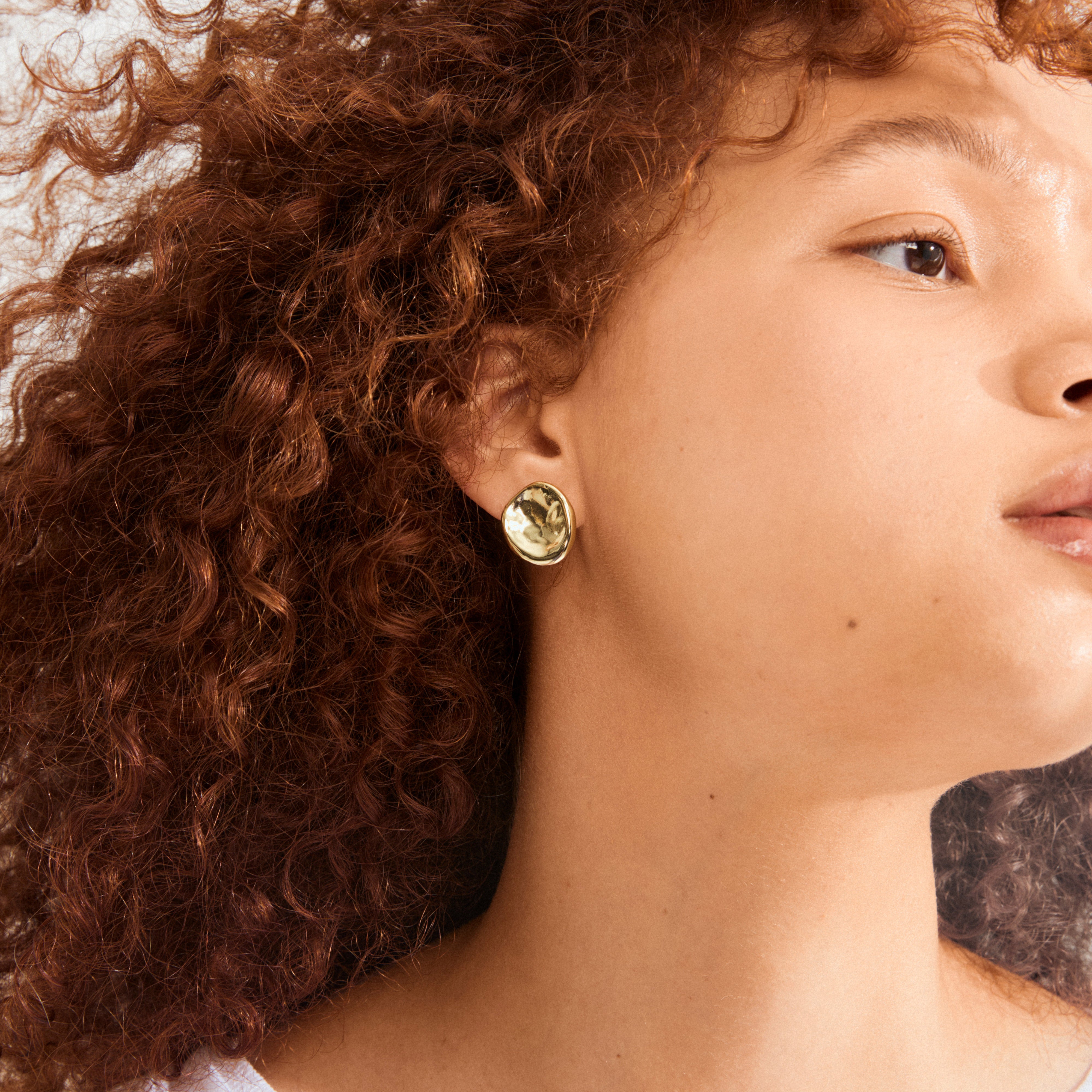 Profile view showcasing SPARKLE earrings gold-plated by Pilgrim, featuring an uneven surface that reflects light, embodying a raw, classy style and sustainable craftsmanship.