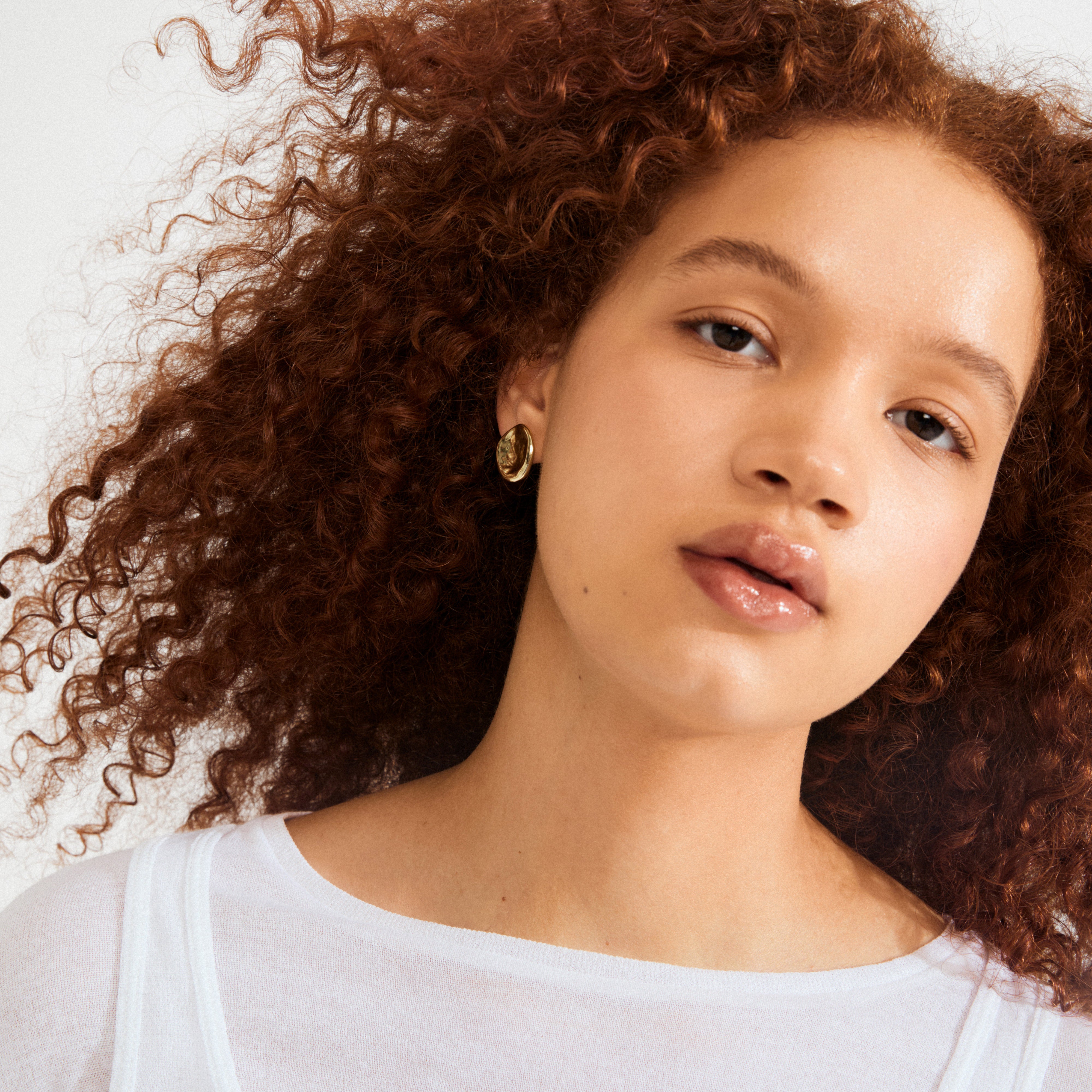Close-up of a young person wearing Pilgrim's SPARKLE gold-plated earrings, showcasing their unique uneven surface that captures light, embodying a raw, classy vibe.