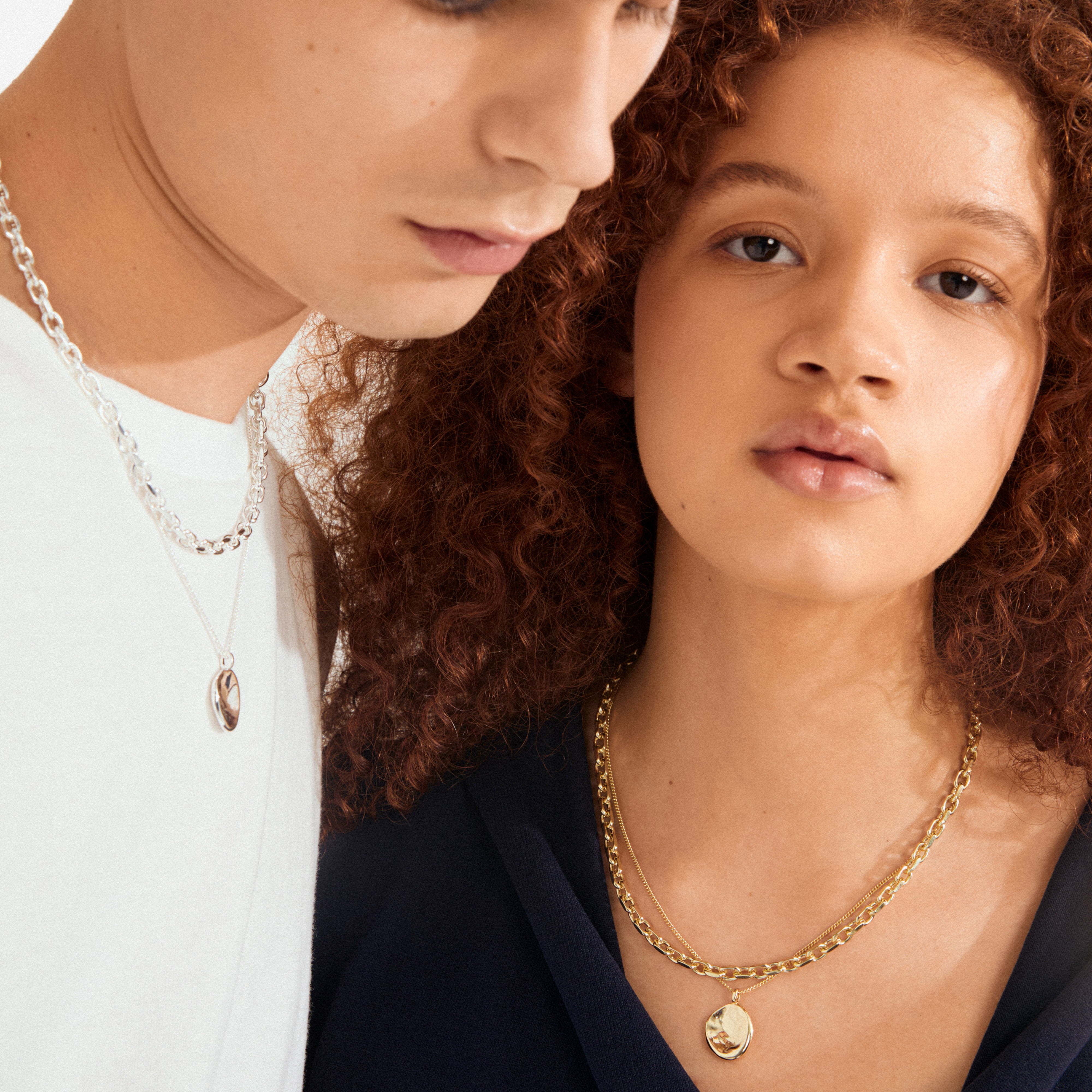 Two young adults showcase Pilgrim's SPARKLE necklace 2-in-1 set, gold-plated, featuring layered gold chains with round pendants, highlighting trendy, personalized style.