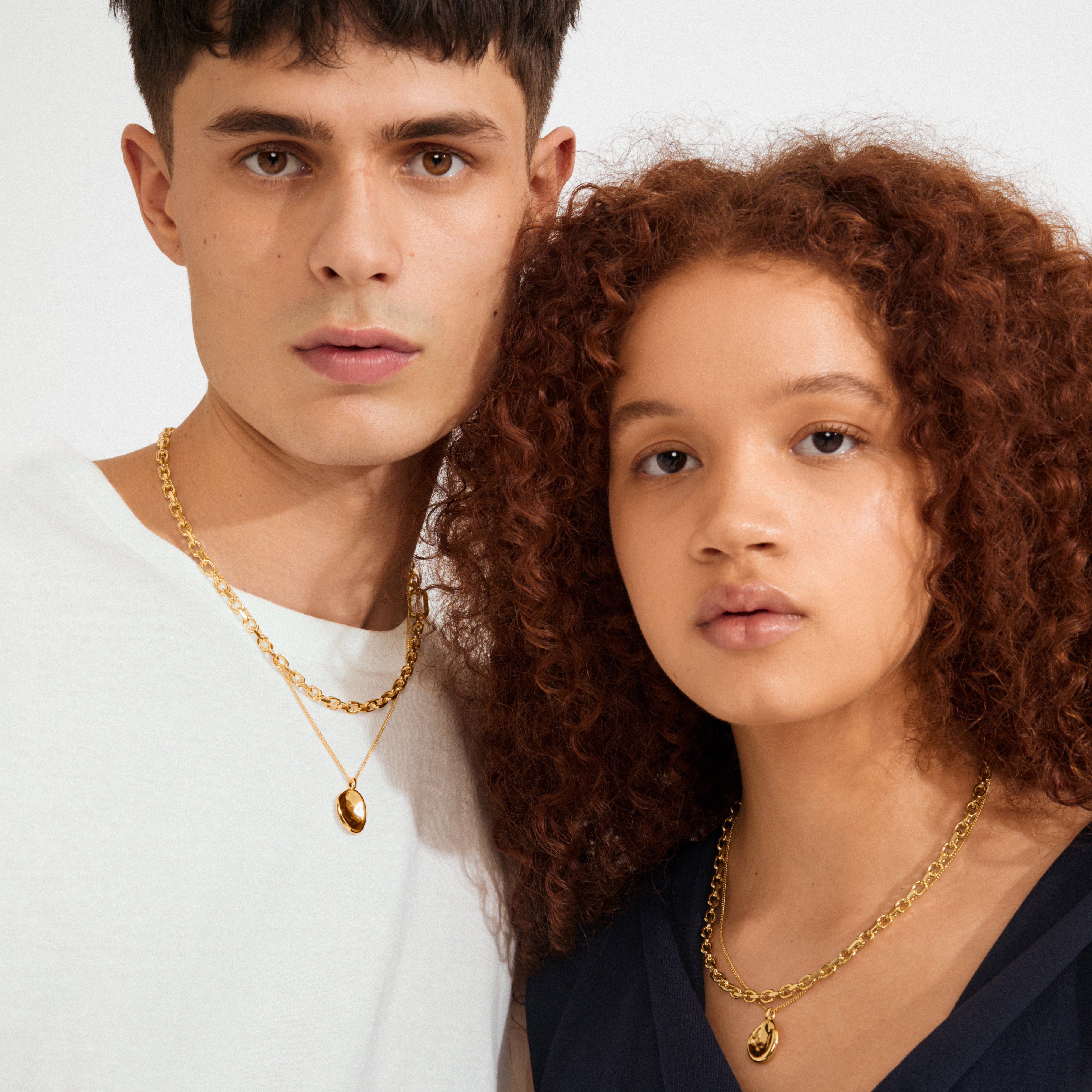 Two models showcase Pilgrim's SPARKLE necklace 2-in-1 set, gold-plated, with chunky chains and oval pendants, highlighting minimalist elegance and personal style.