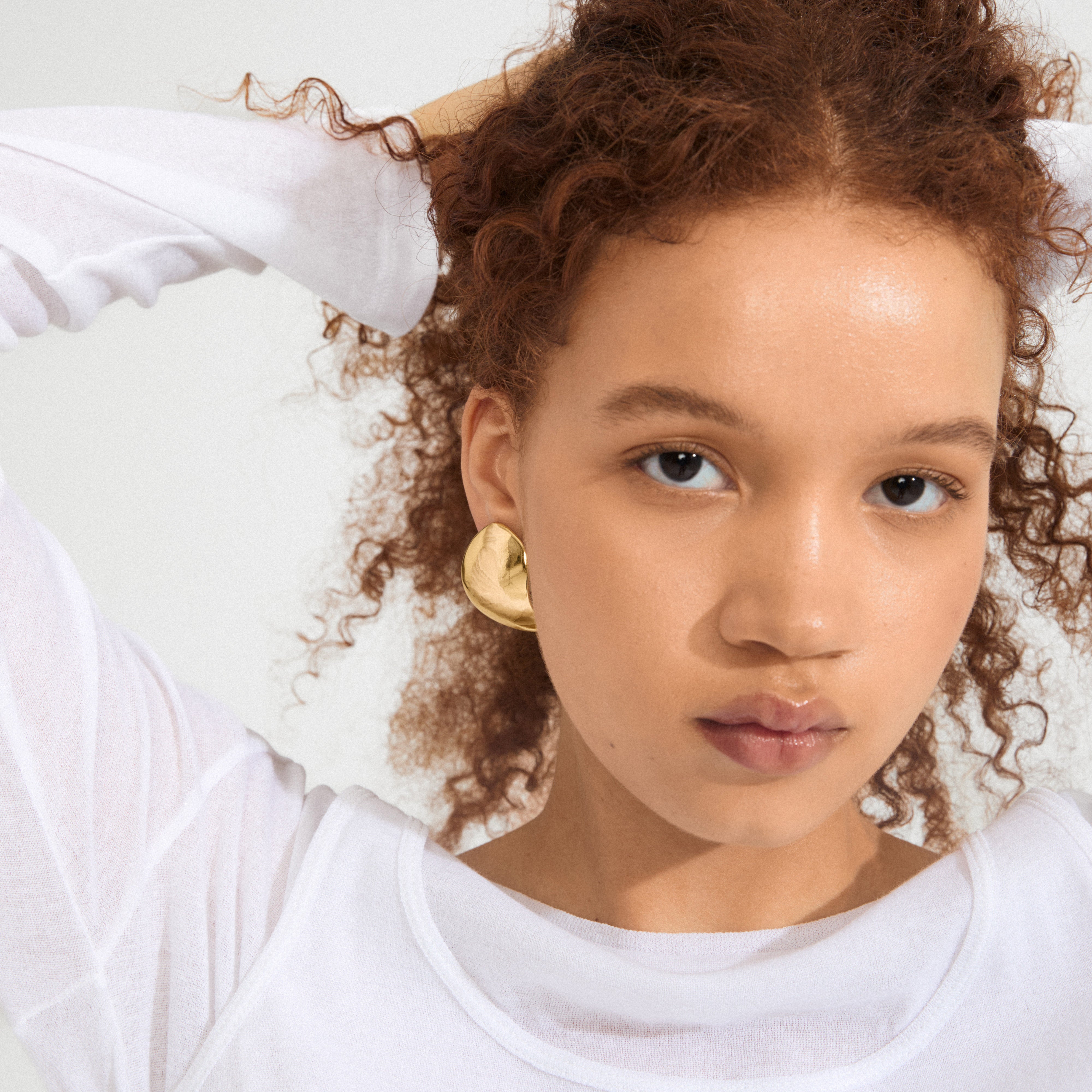 A young person wears SPARKLE earrings gold-plated, showcasing a sculptural design that embodies Pilgrim's blend of trendy and timeless Danish craftsmanship.