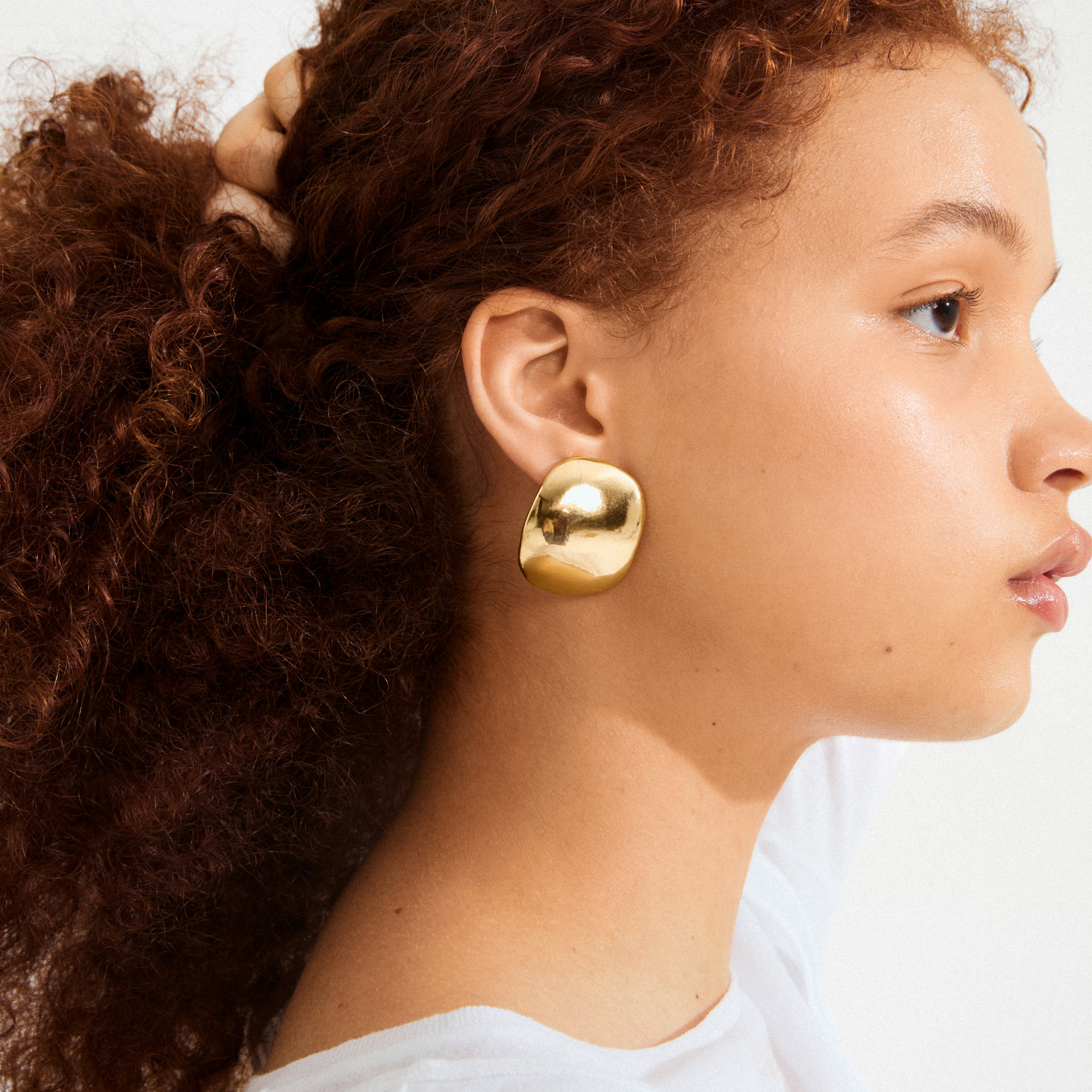Side profile of person wearing SPARKLE earrings gold-plated, showcasing large, polished gold stud with sleek, voluminous design, highlighting Pilgrim's blend of trendy and timeless style.