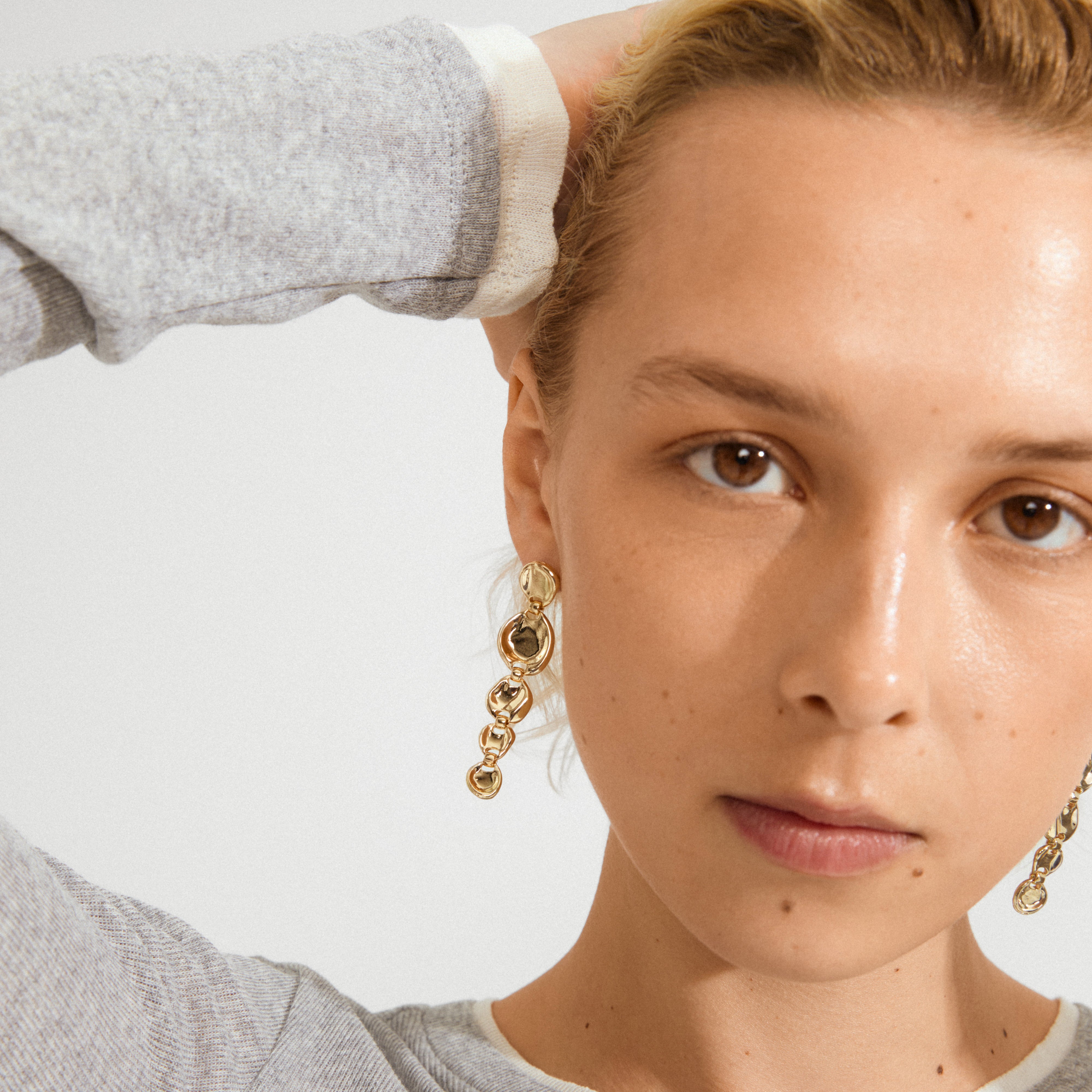 Young person wearing SPARKLE earrings gold-plated by Pilgrim, featuring dangling chain of linked circles, adding vintage flair and sparkle, perfect for chic and edgy styles.