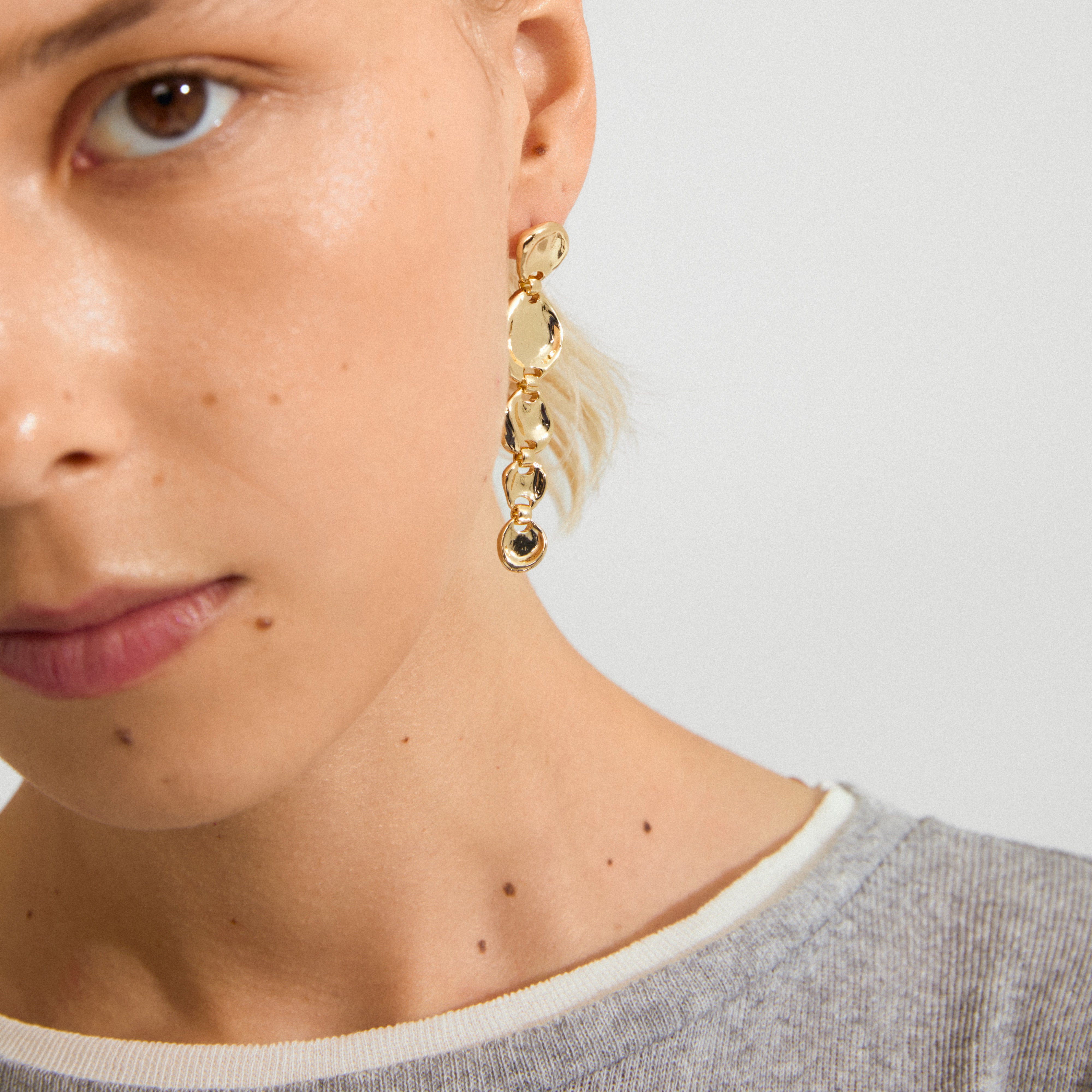 Close-up of SPARKLE earrings gold-plated by Pilgrim, featuring linked, irregular discs on a dangling chain, adding a vintage sparkle to the look.