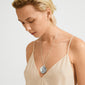 Person wearing a SPARKLE necklace silver-plated by Pilgrim, featuring a long chain and wavy pendant, epitomizing Scandinavian design and sustainability.
