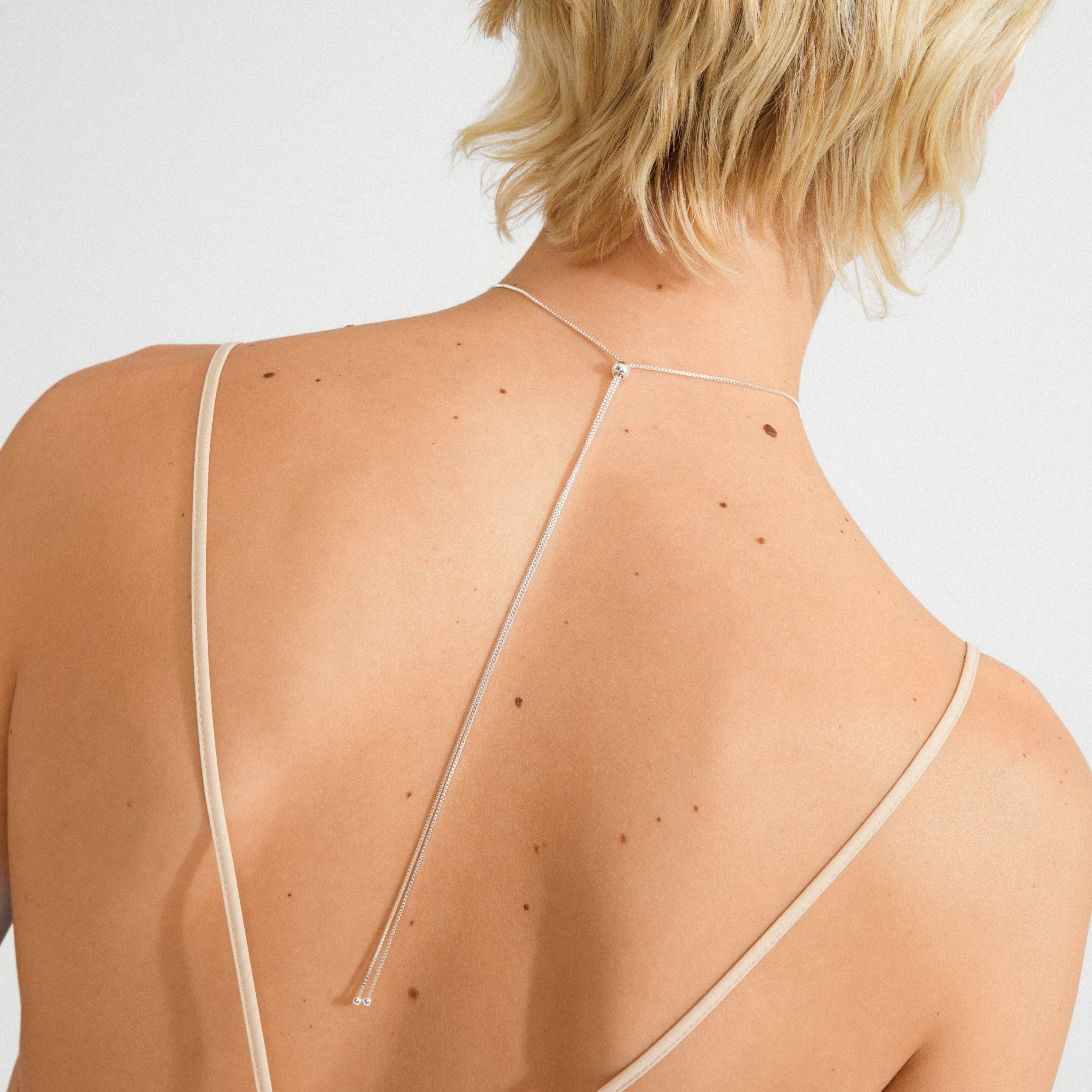 Person wearing Pilgrim's SPARKLE necklace, a silver-plated, Y-style piece with delicate chains and beads, displayed on a freckled back for a minimalist look.
