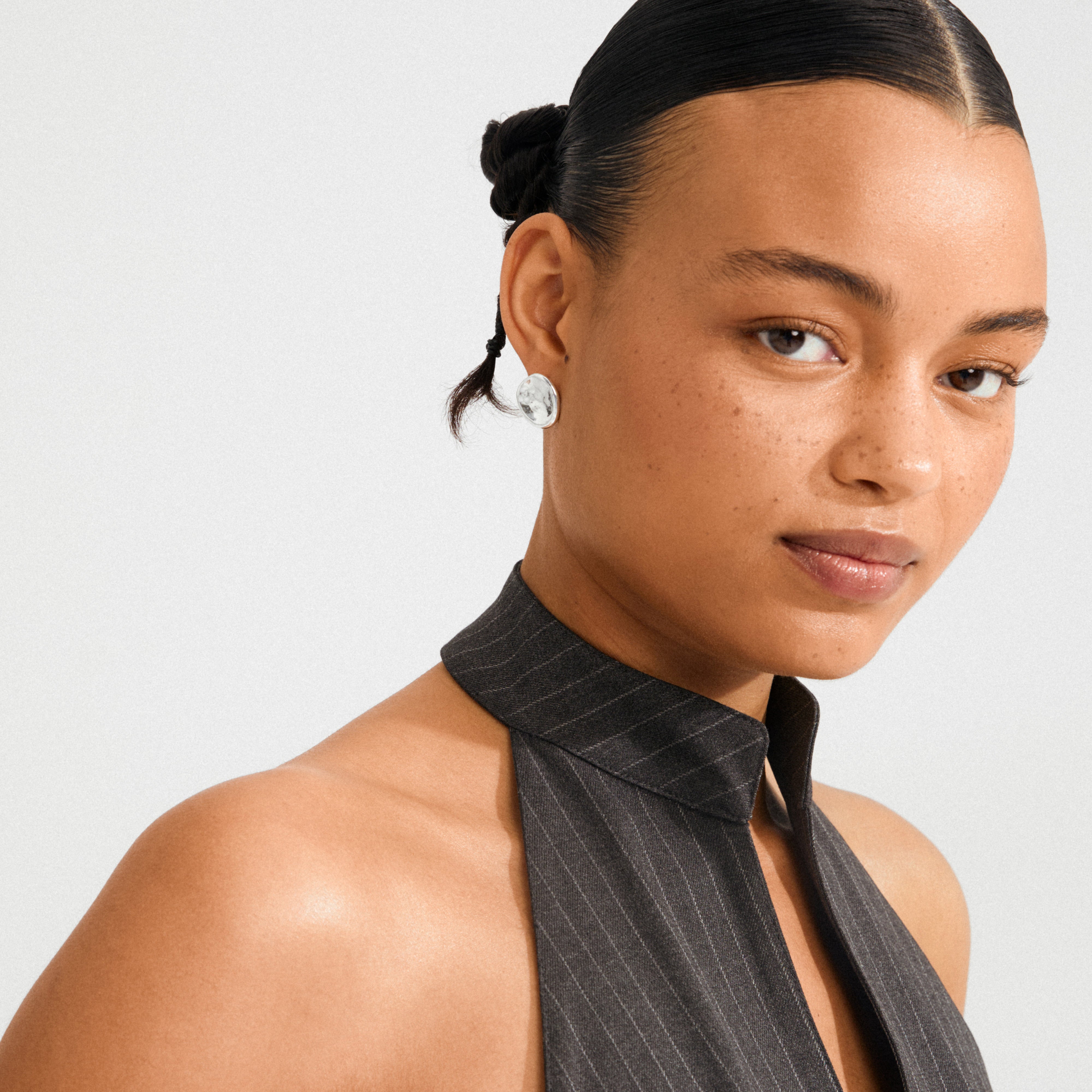 Person wearing SPARKLE earrings, silver-plated studs with a textured surface, showcasing minimalist style and Scandinavian craftsmanship. Hair styled in buns with a braid.