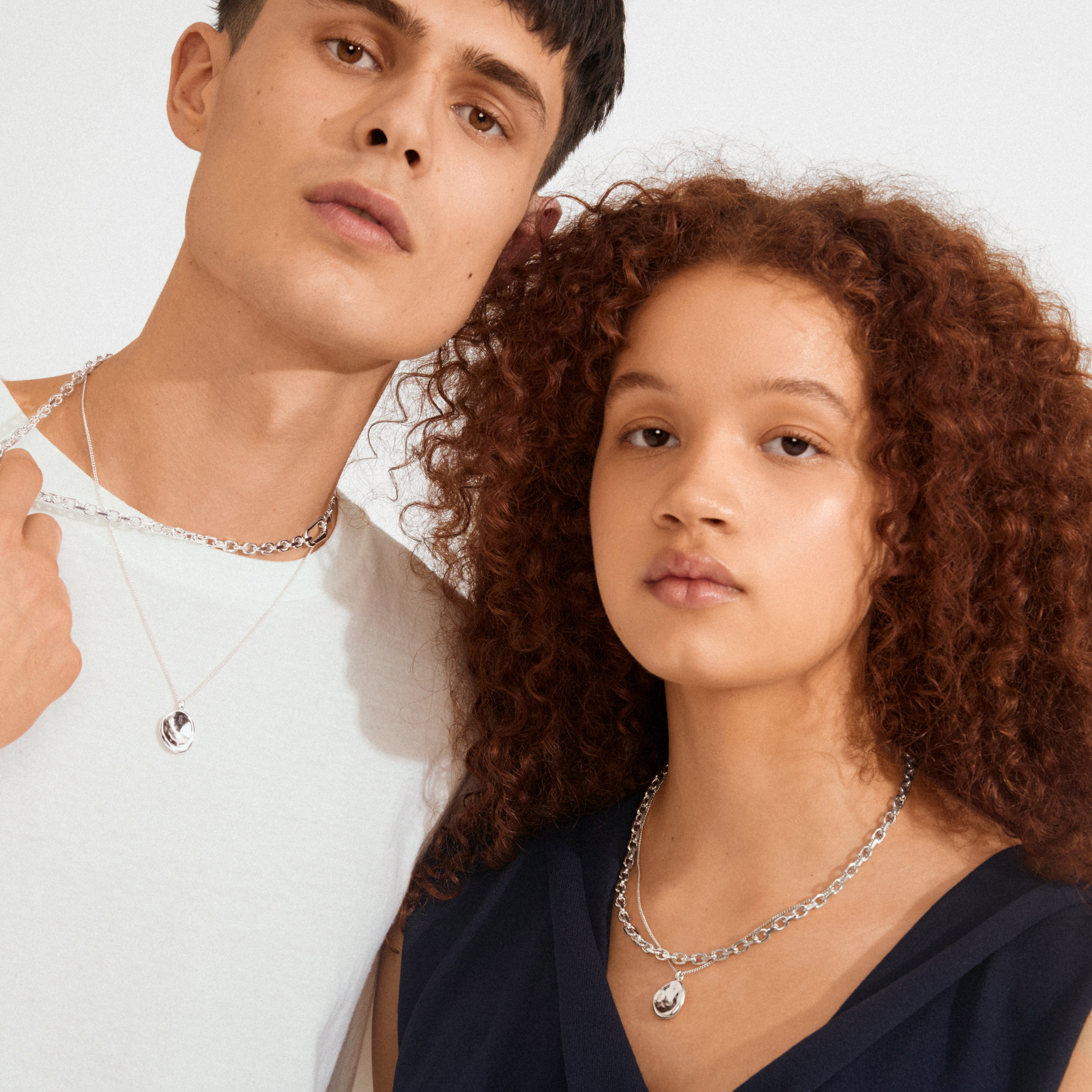 Two young adults showcase Pilgrim's SPARKLE necklace 2-in-1 set, featuring silver-plated chains with round pendants, embodying minimalism and elegance.