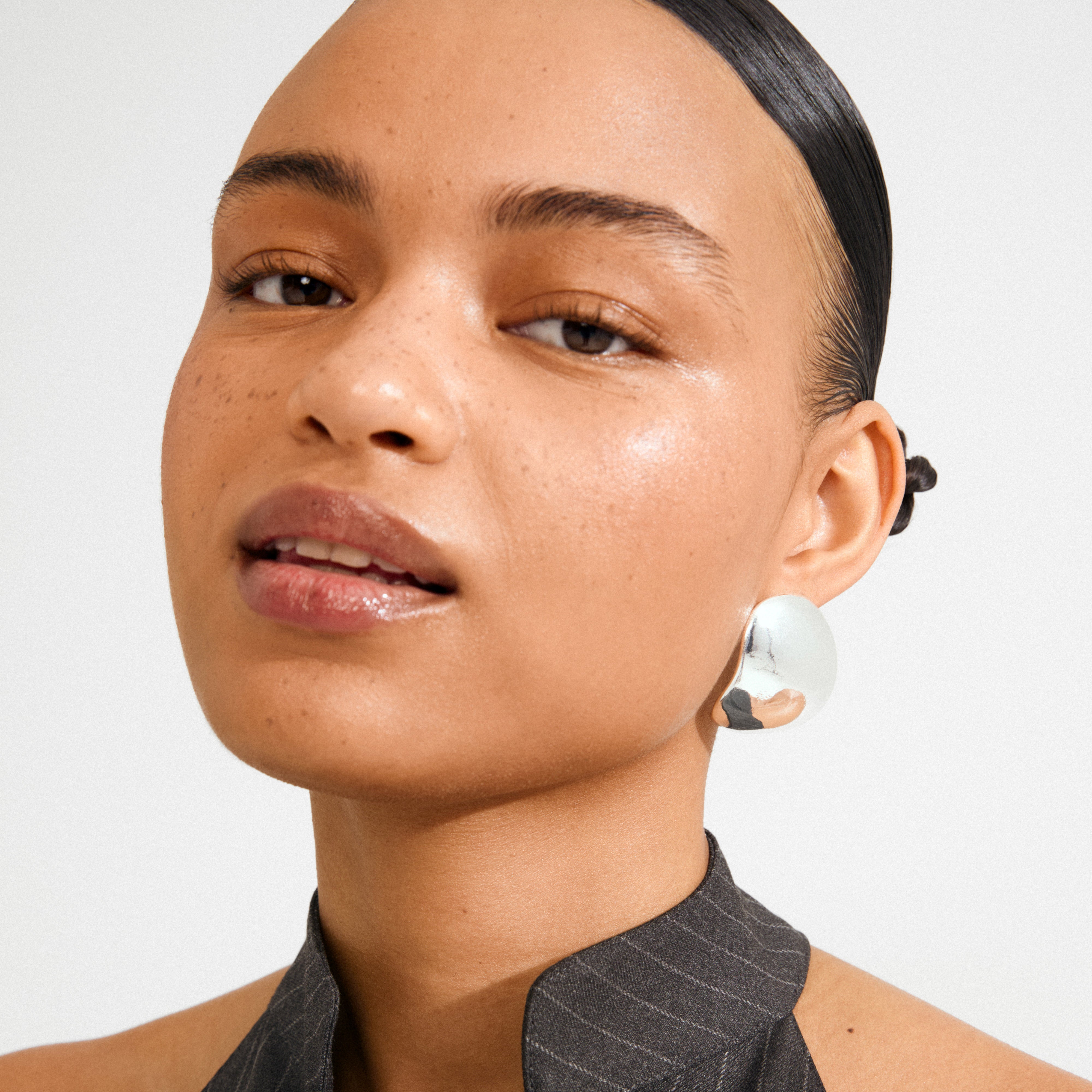 Portrait featuring SPARKLE earrings silver-plated by Pilgrim, showcasing sleek, chunky silver design on a young person with pulled-back hair and pinstriped top.