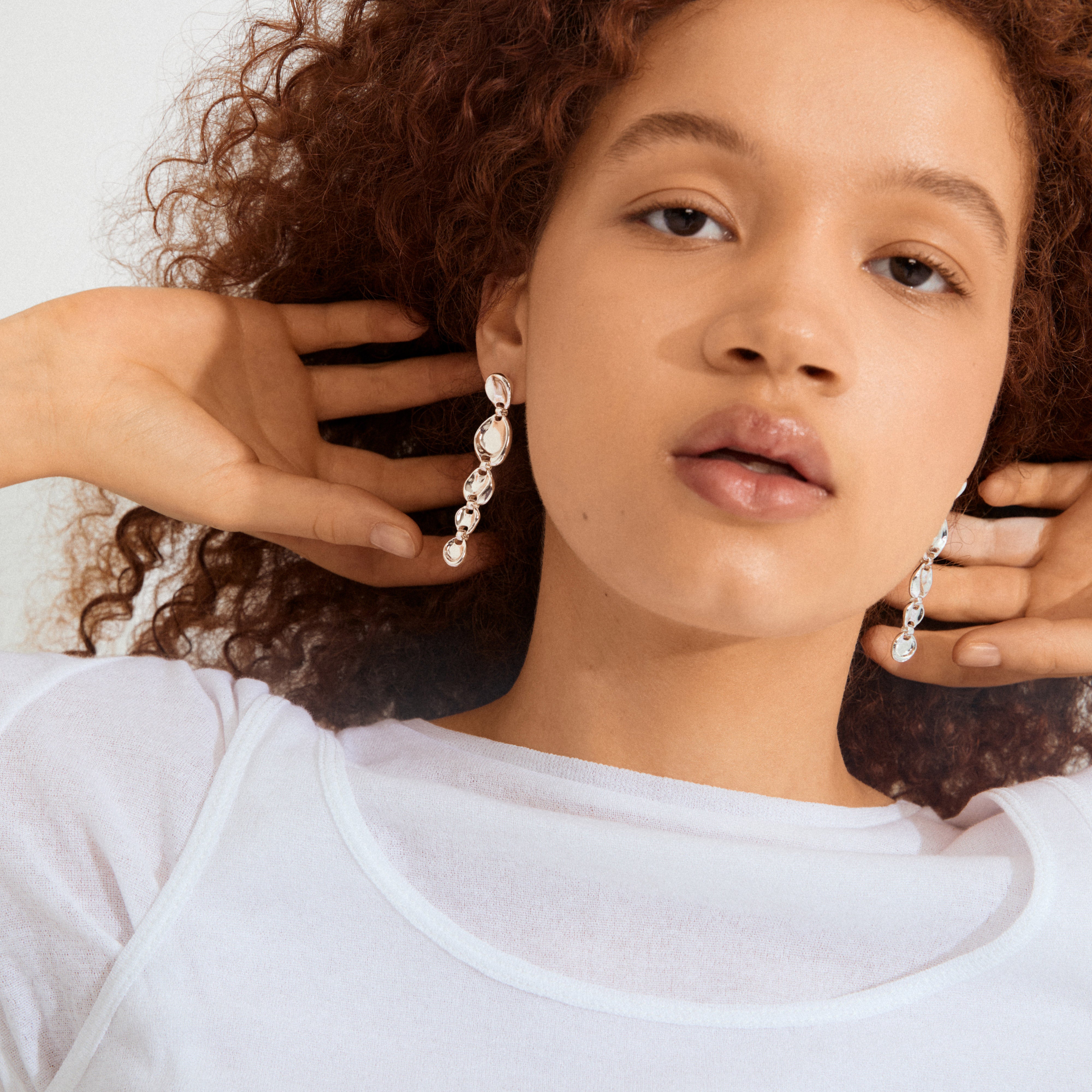 Model with curly hair wearing SPARKLE earrings silver-plated, featuring pebble-shaped links, highlighting their vintage-inspired, textured design, perfect for chic, everyday elegance.