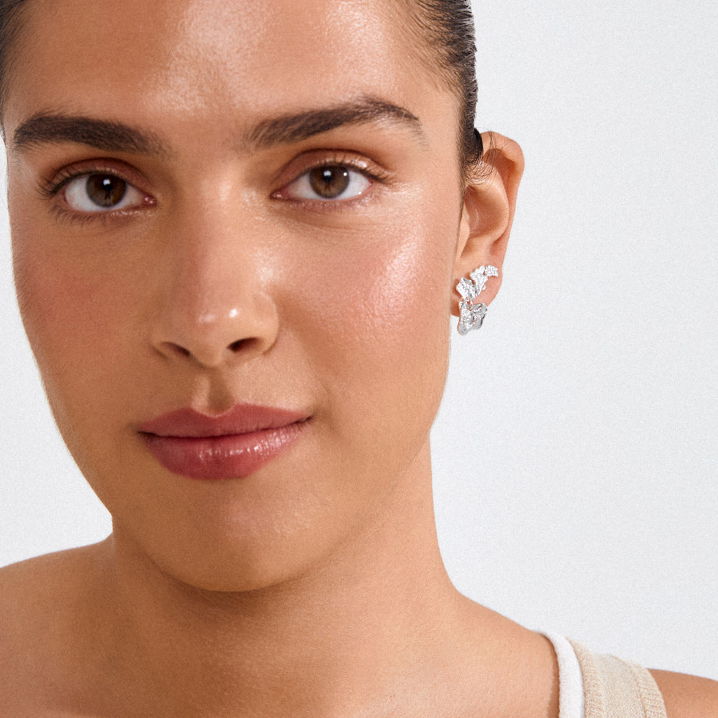 Young woman wearing HORIZON earrings silver plated, featuring a sculptural, molten-metal texture, showcasing an elegant and modern look with natural makeup and pulled-back hair.