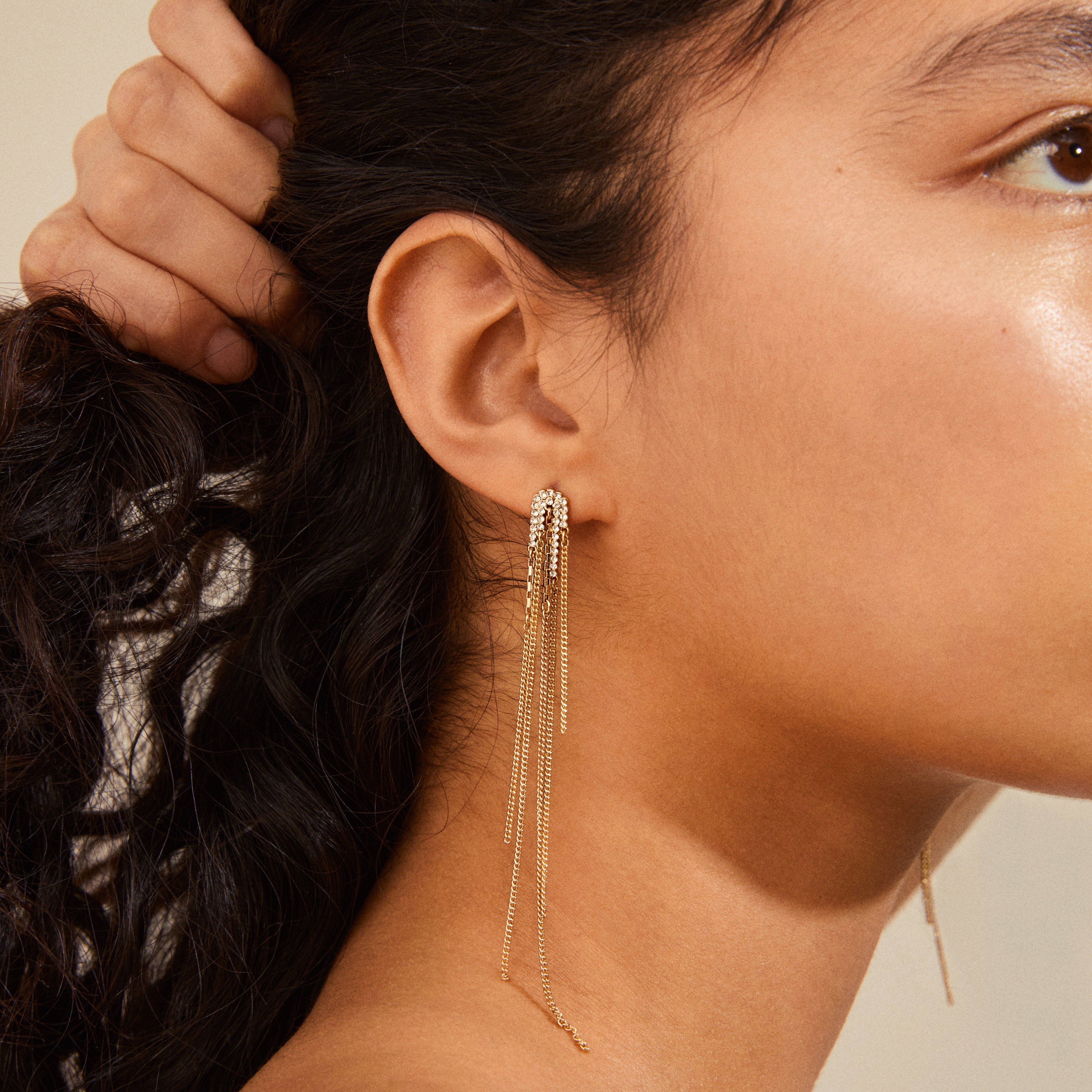 Close-up of a gold-plated Serenity earring from Pilgrim, featuring cascading fine chains and sparkling crystals, inspired by nature's elegance.