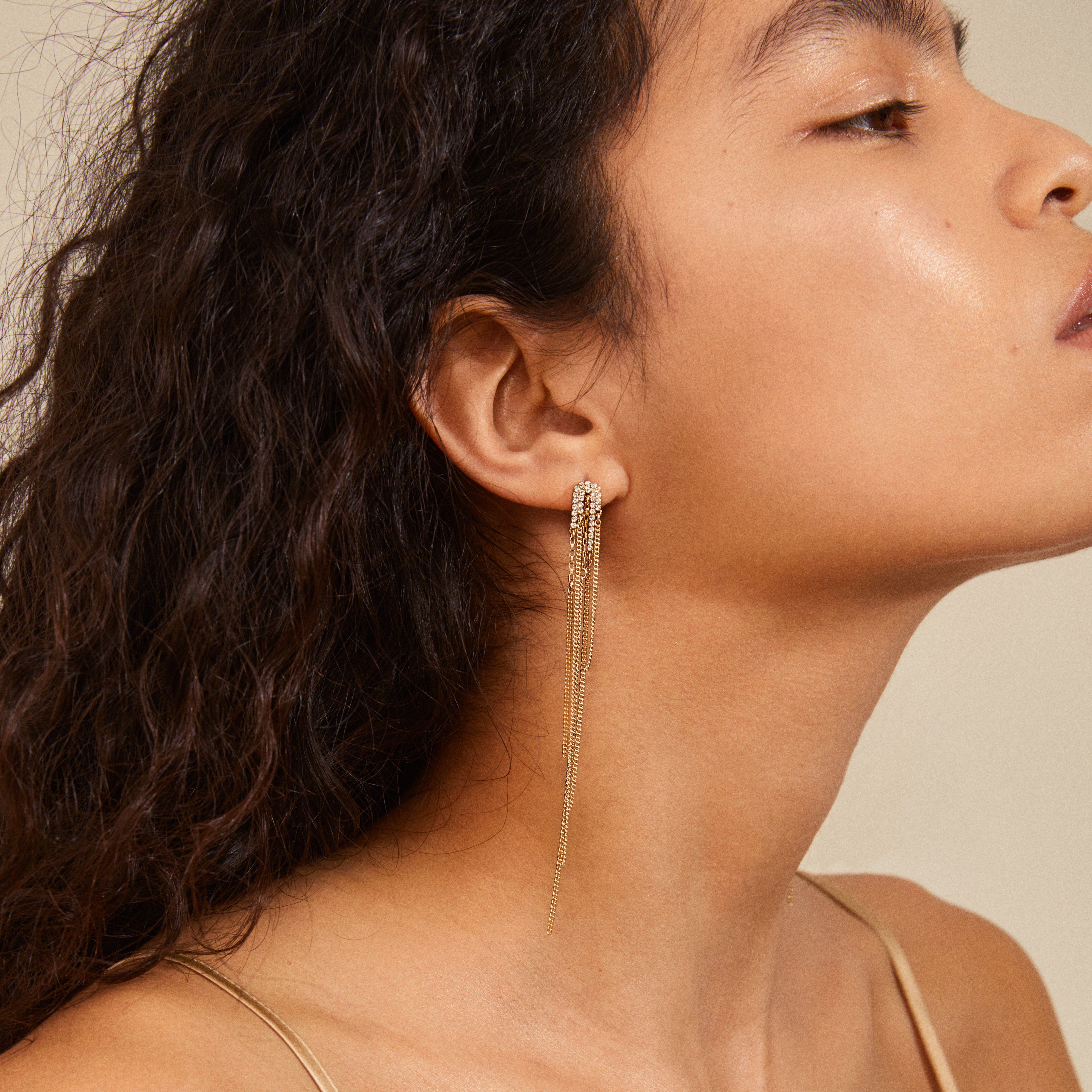 SERENITY crystal deco waterfall earrings in gold-plated design; features rhinestone cluster studs with tassel chains, showcased on a woman's side profile with pulled-back hair.