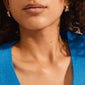 WILLPOWER huggie hoop earrings gold-plated, showcasing Nordic design with organic-embossed texture, worn by a model highlighting natural skin texture and a ribbed blue top.