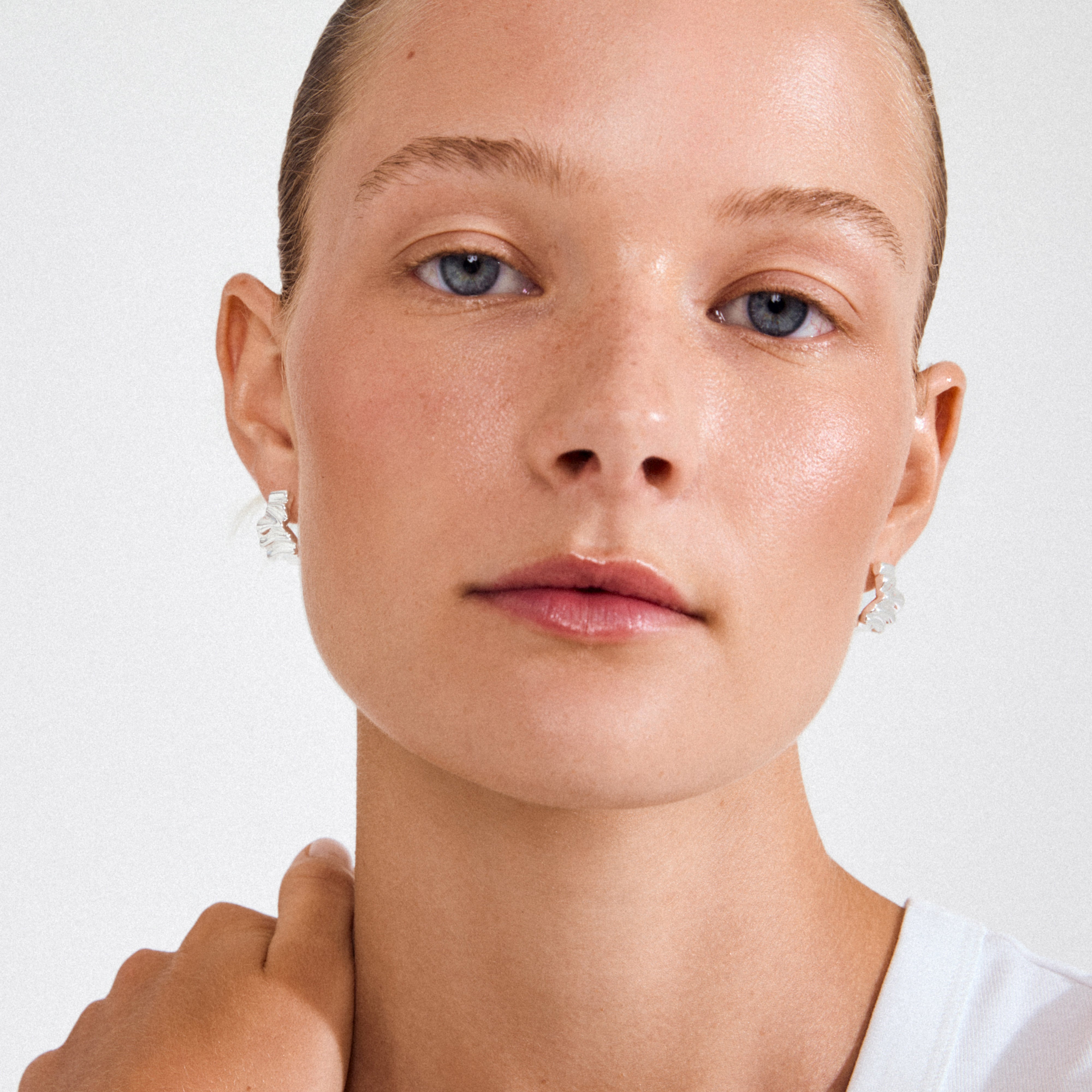 Young woman wearing Pilgrim’s WILLPOWER silver-plated huggie hoop earrings, showcasing their twisted-metal design, crafted from 99% recycled materials.