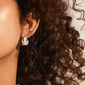 Close-up of dark, curly hair showcasing WILLPOWER huggie hoop earrings, silver-plated with a sculptural, handcrafted design, highlighting Pilgrim's commitment to recycled materials.