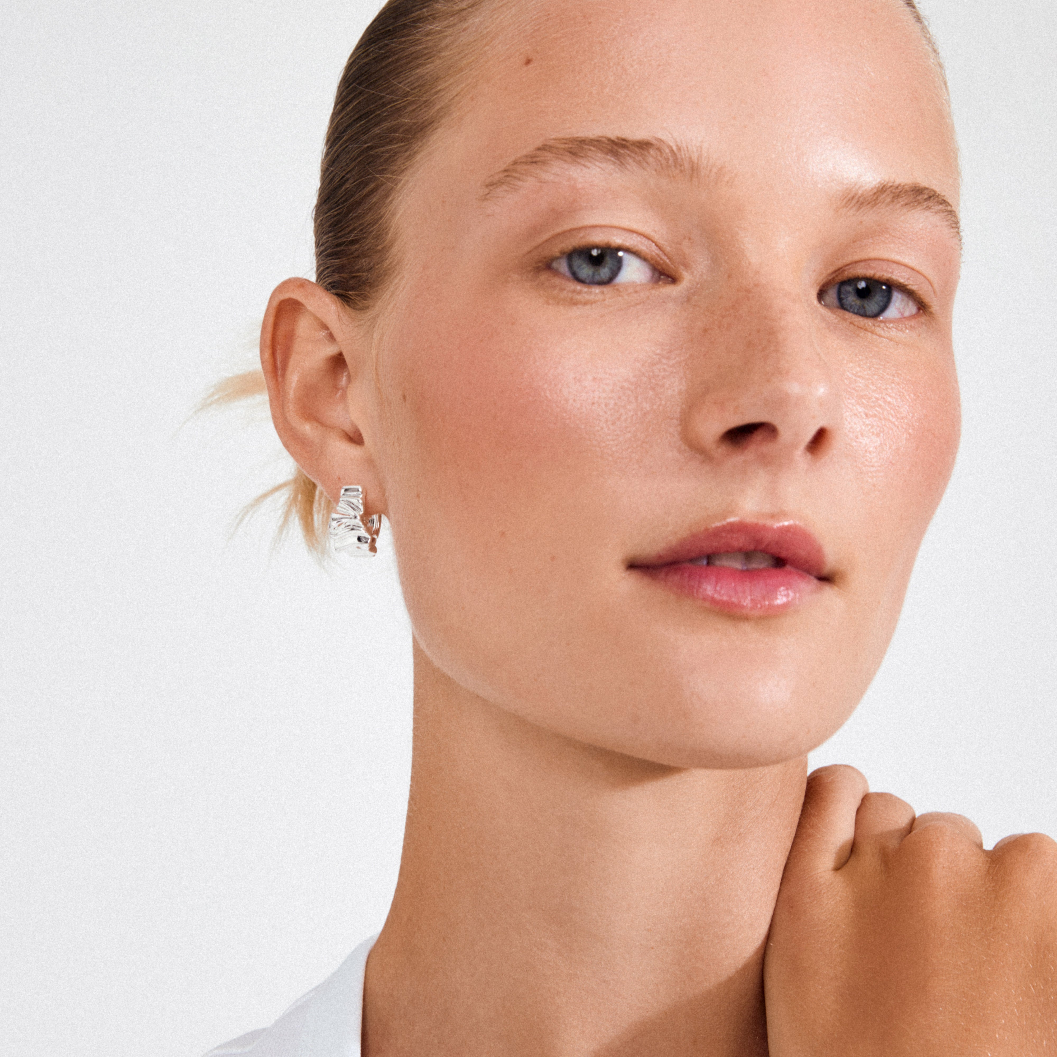 Young woman wearing WILLPOWER huggie hoop earrings, silver-plated with wavy, textured design. Earrings crafted from 99% recycled materials, adding a natural edge to her style.