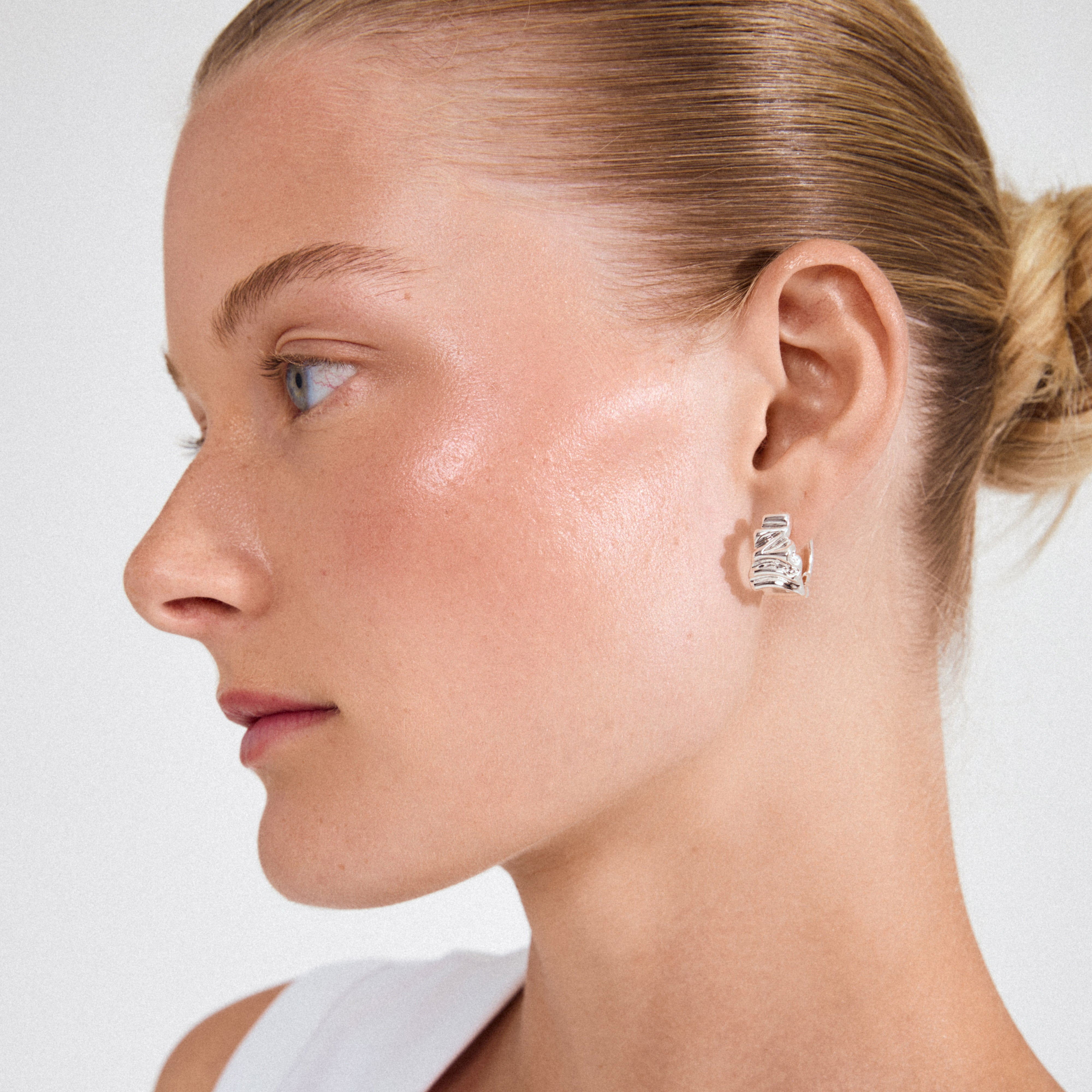 Close-up of a woman wearing WILLPOWER huggie hoop earrings, showcasing their sculptural, silver-plated design, crafted from recycled materials, blending nature-inspired shapes with classic hoops.