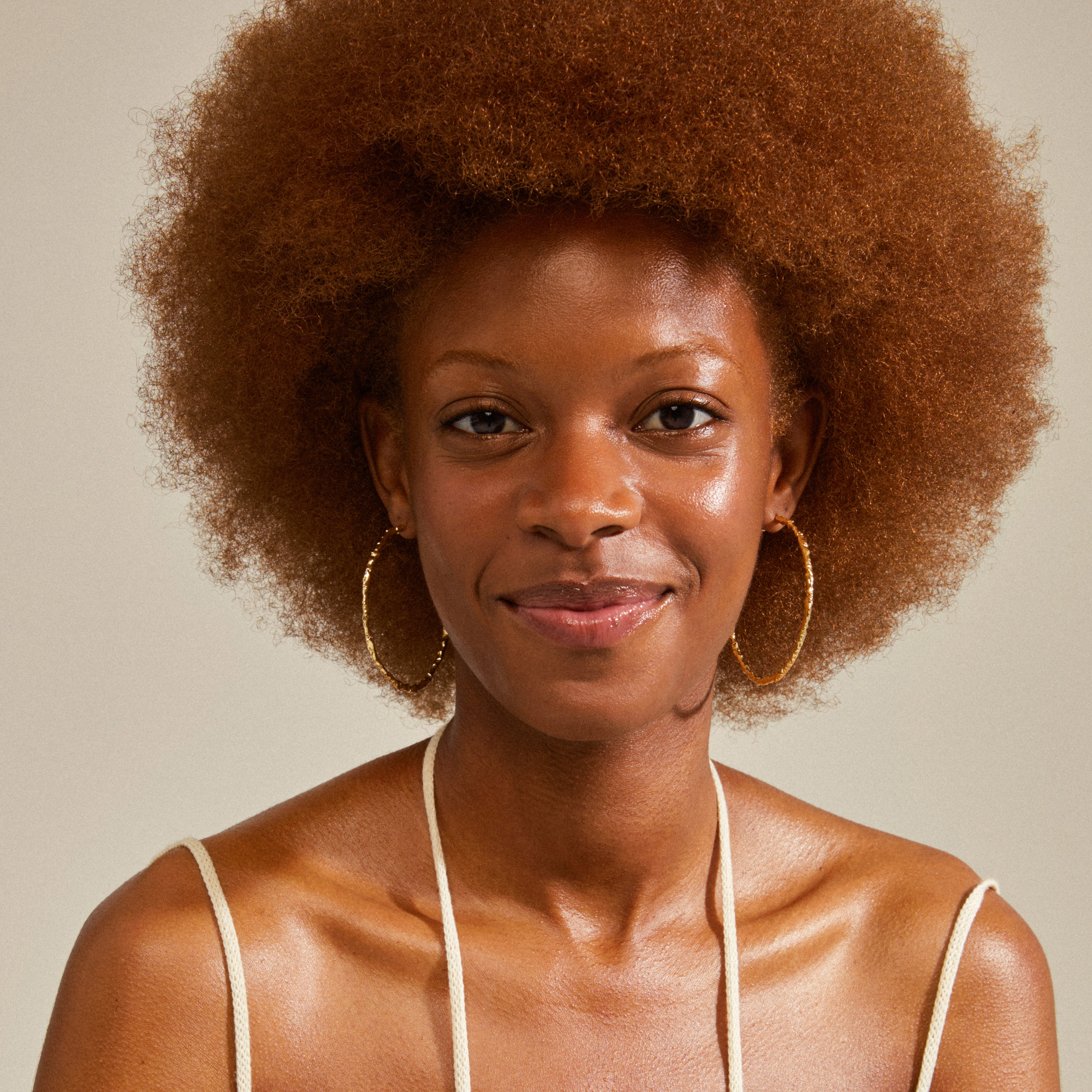 Smiling woman wearing SUN mega hoops gold-plated by Pilgrim, showcasing their large, uneven, organic design.
