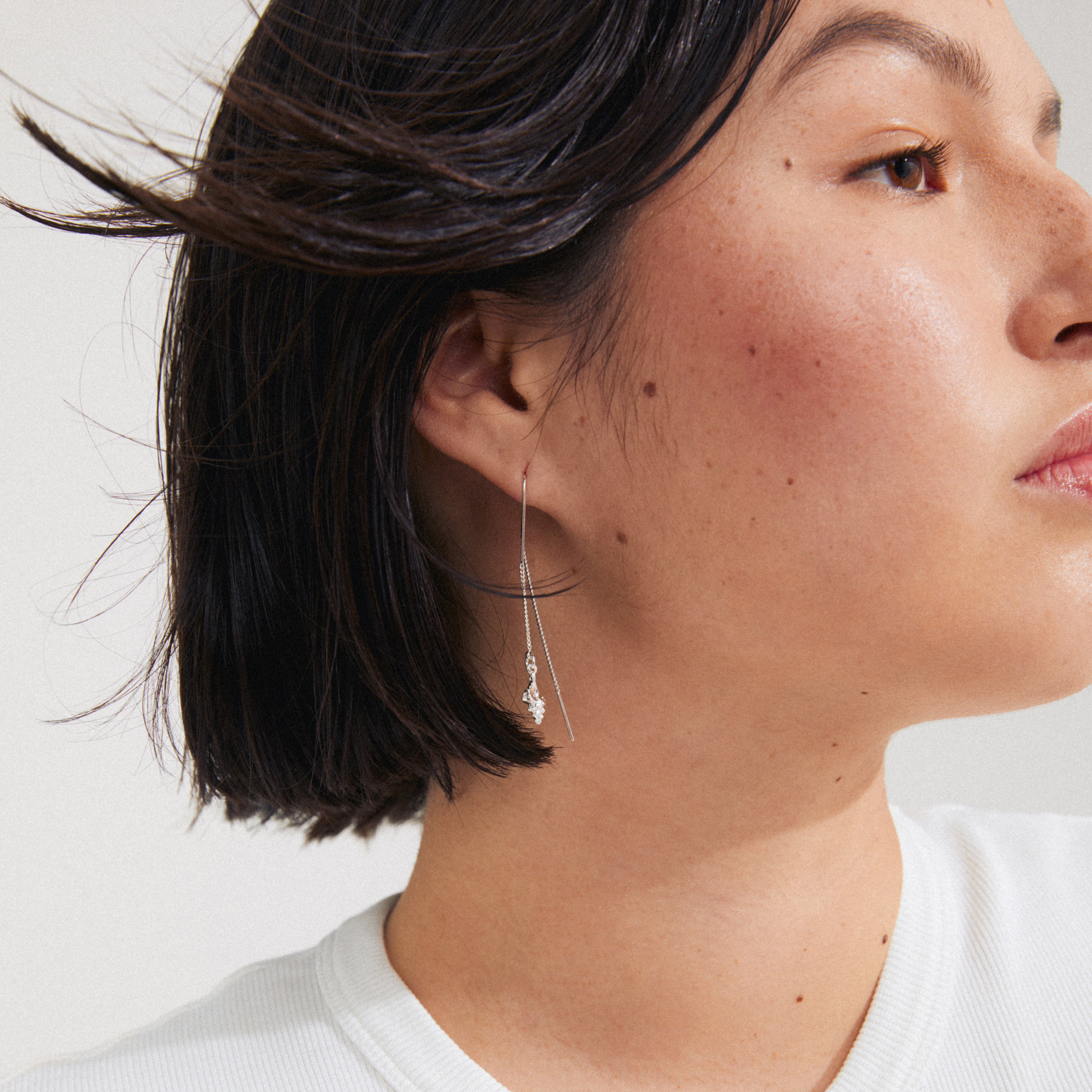 Silver-plated SEA chain earrings with tiny conch shells, styled on a woman with short hair, enhancing a summer vibe. Perfect for a trendy, curated ear look.